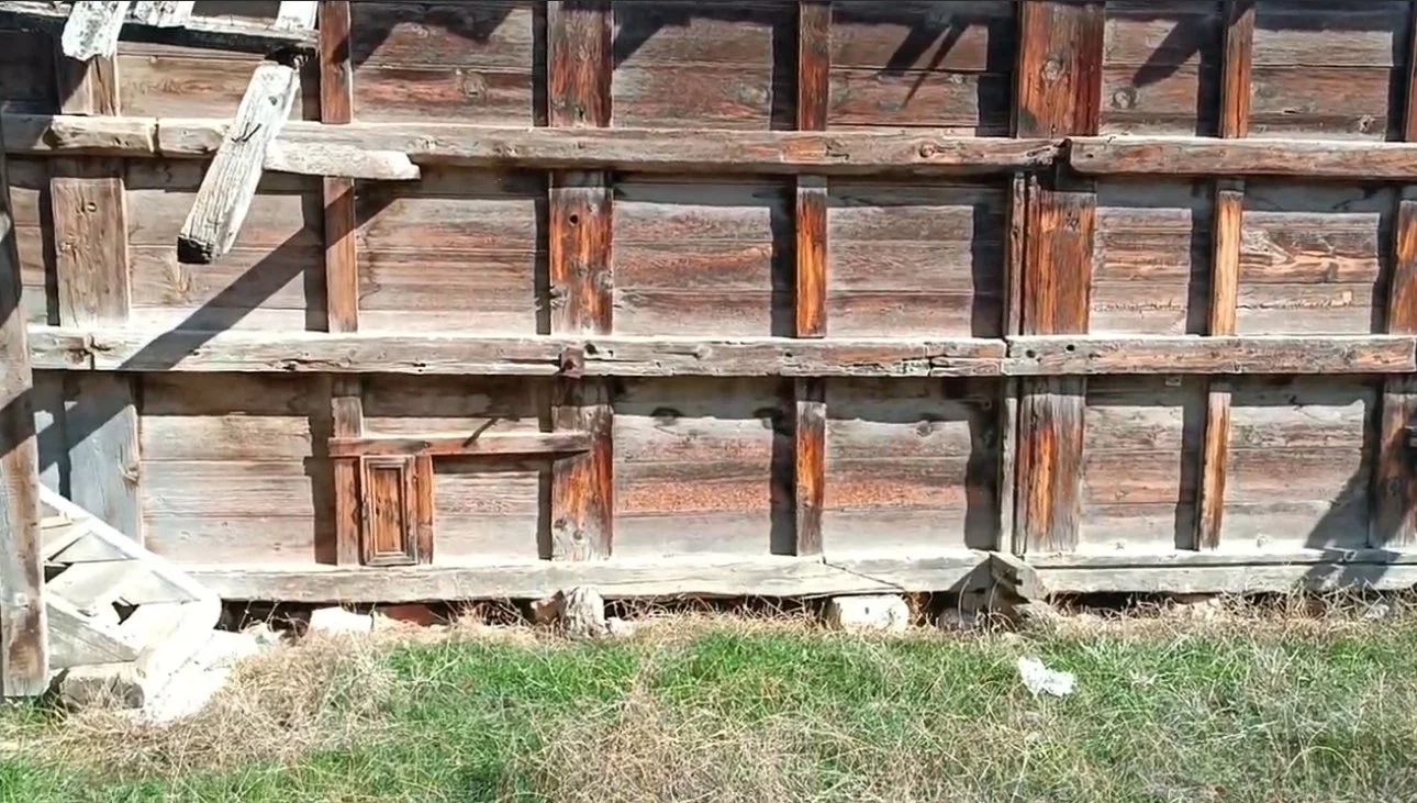 Ahşap raylar ve tahtalarla yapılan eski bir yapı, zemin üzerinde biraz ot ve taşlar bulunuyor.