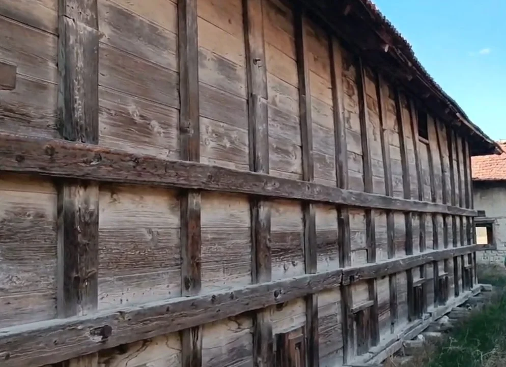 Ahşap büyükce eski bir bina, taş temel üzerinde bulunuyor, yanlarda küçük pencereler var.