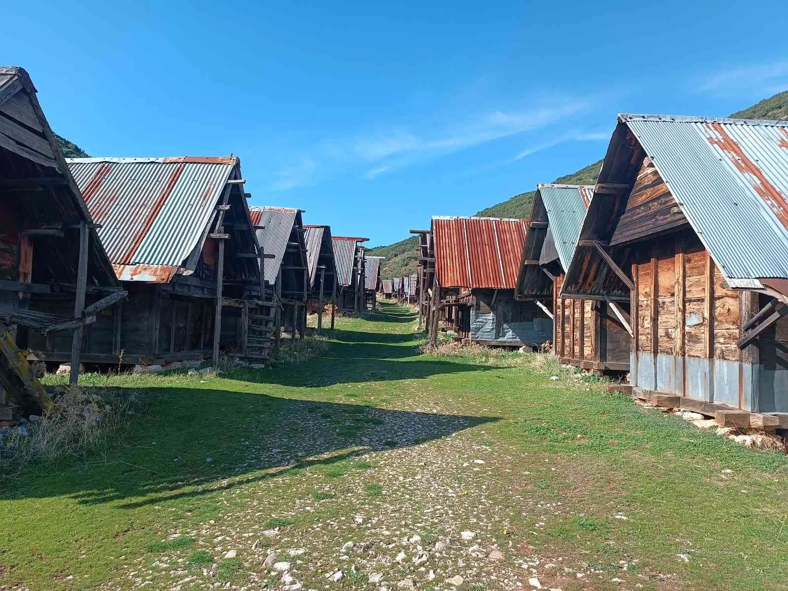 Dağ manzarasıyla küçük, ahşap ve çatıları metal olan evler veya kulübeler sıralanmış.
