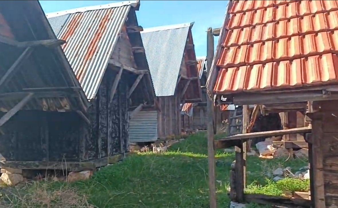 Dikdörtgen ve kiremit çatılı, ahşap evler, yeşil çim alan, açık gökyüzü.