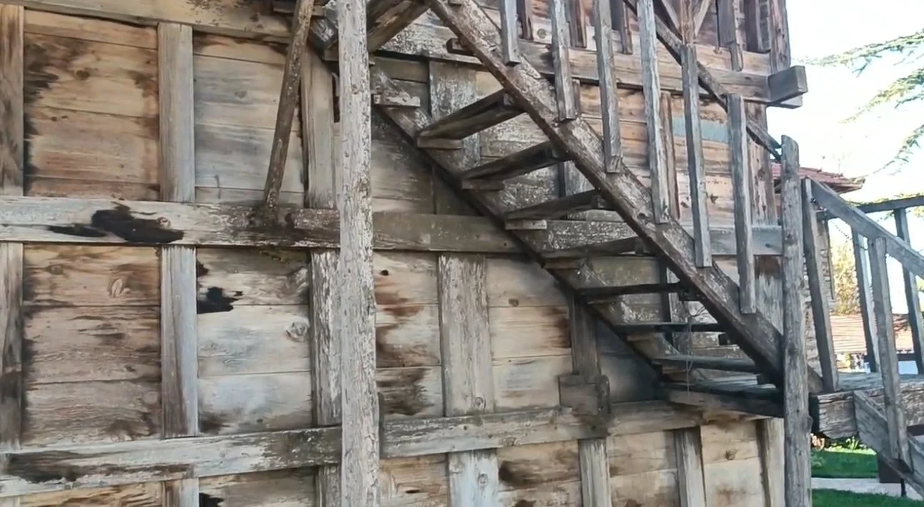 Ahşap bir merdiven ve bina duvarı, iki katlı eski ve bakımsız görünümde.