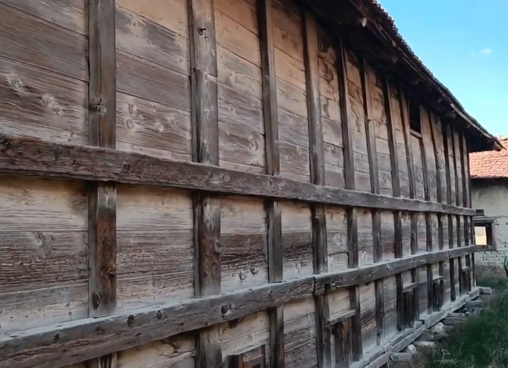 Ahşap çiftlik evi duvarı, acrosslamalar ve pencereler görünmekte.