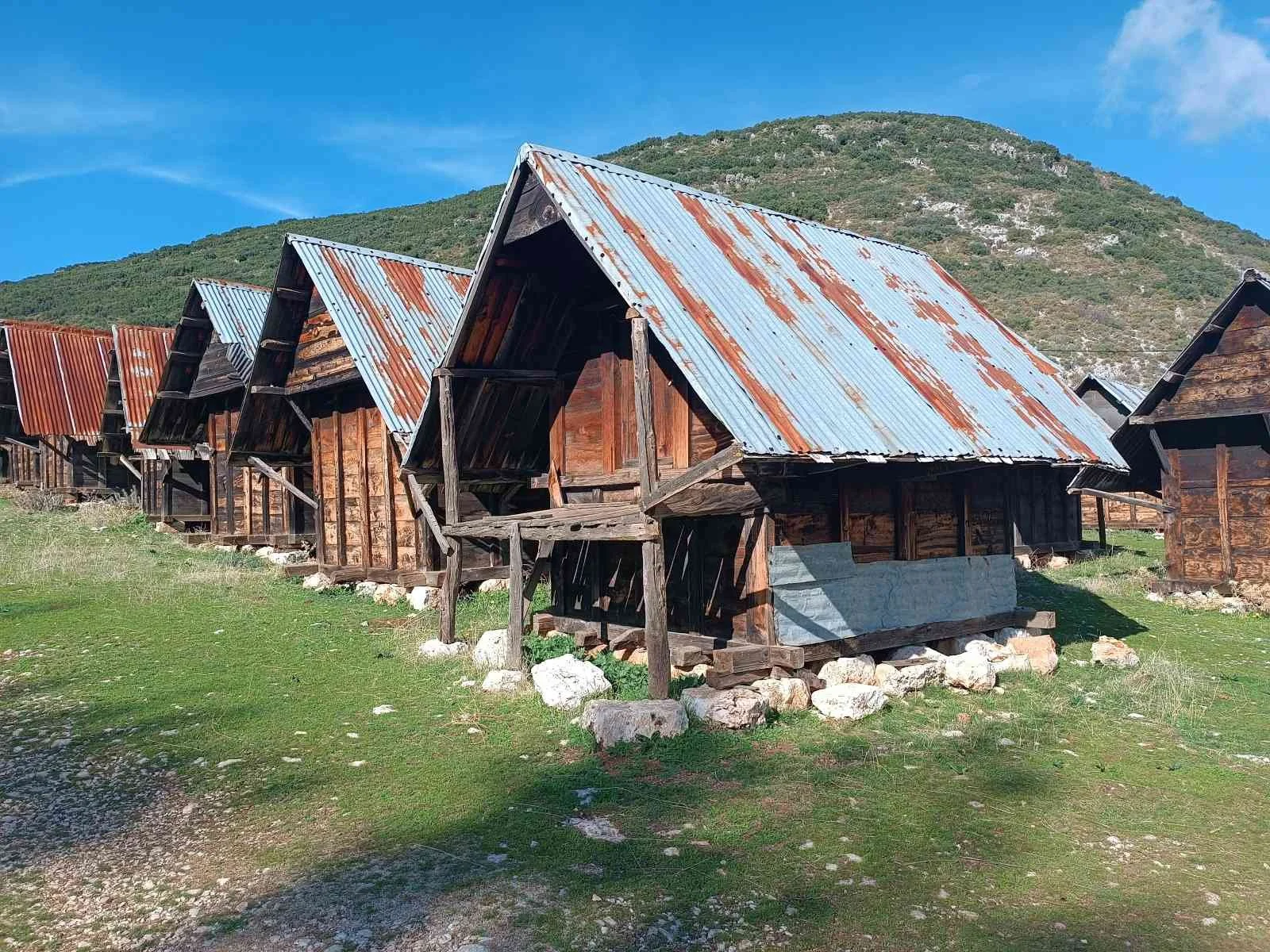 Tarz malzemeleriyle yapılmış, ahşap ve metal çatıya sahip geleneksel köy evleri, yeşil alan ve dağ manzarasıyla