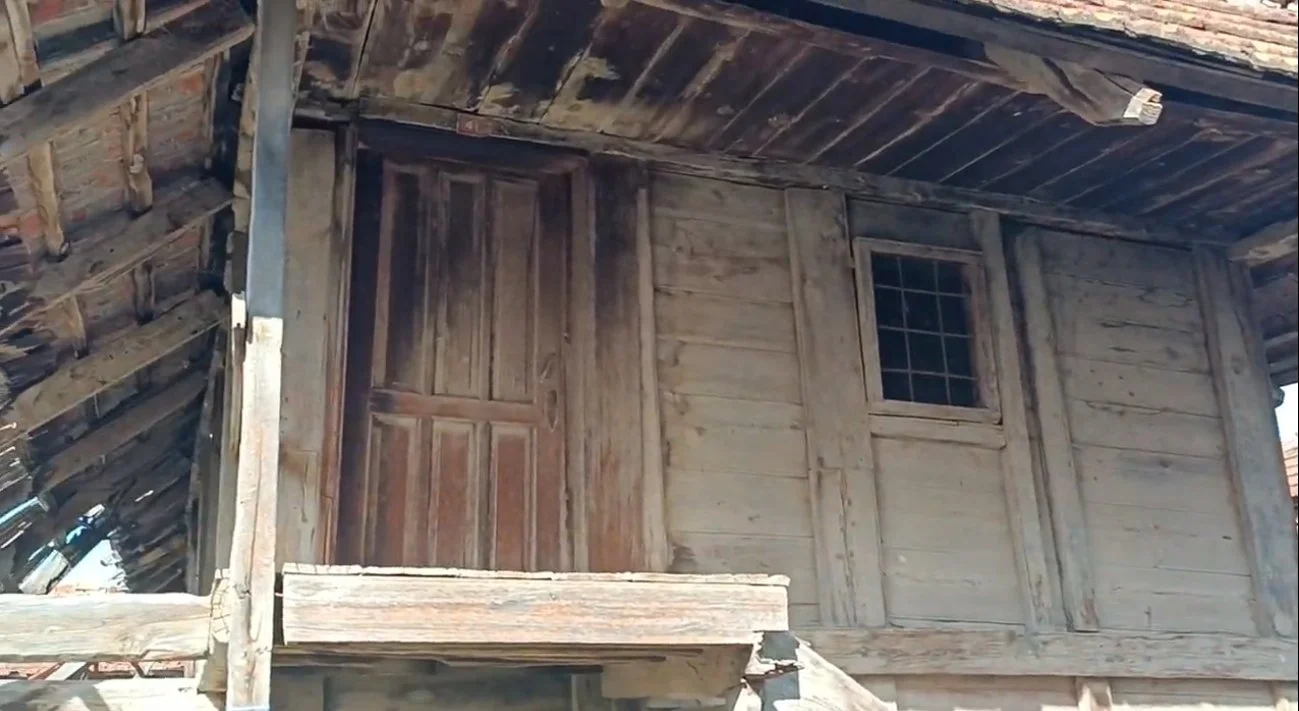 Eski tahta yapı, kapı ve pencere ile ahşap duvarlar, çatıda eğik tahta kiremitler.