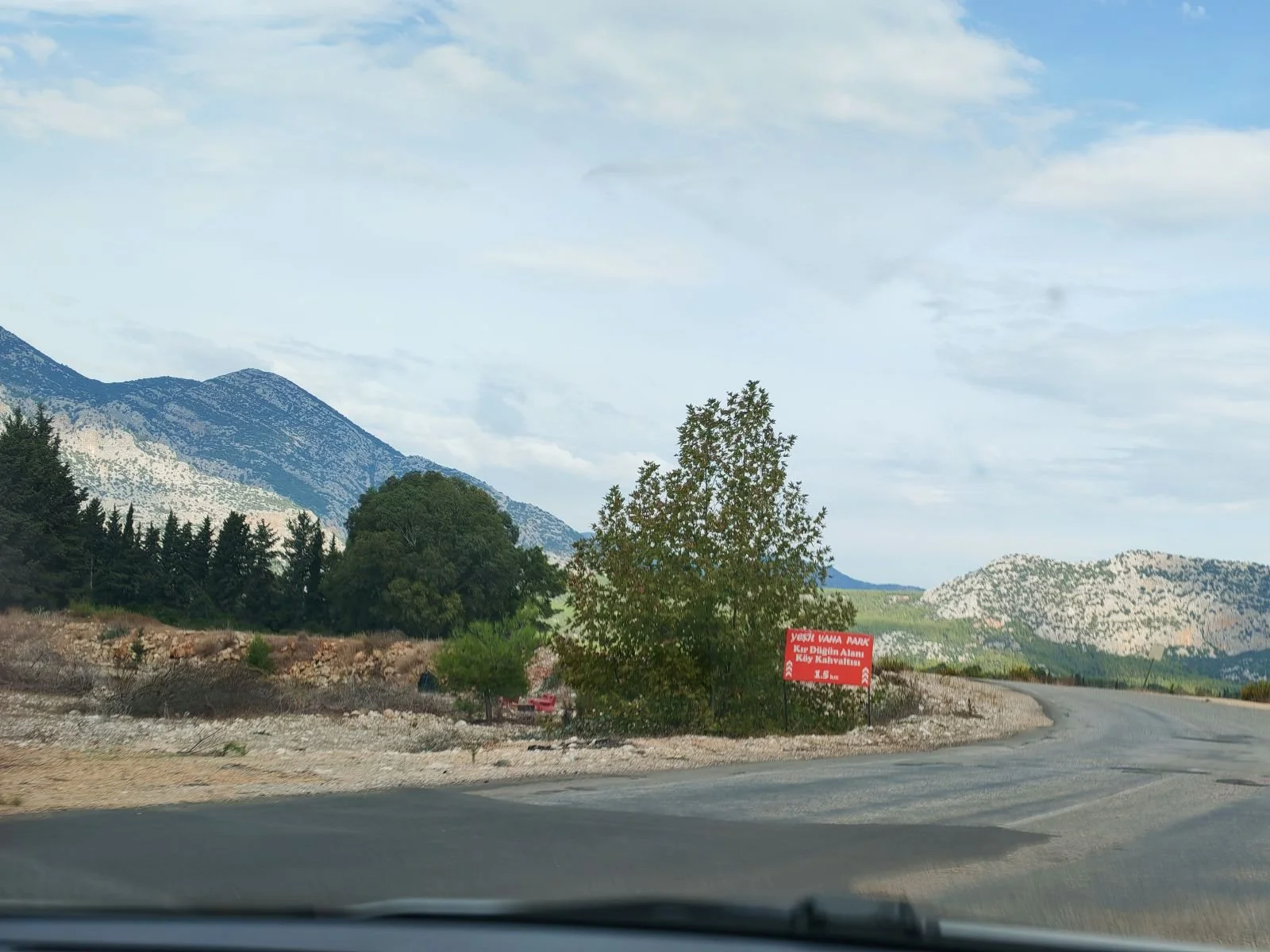 Dağlar ve ağaçlar ile bir yol ve kırmızı uyarı tabelası.