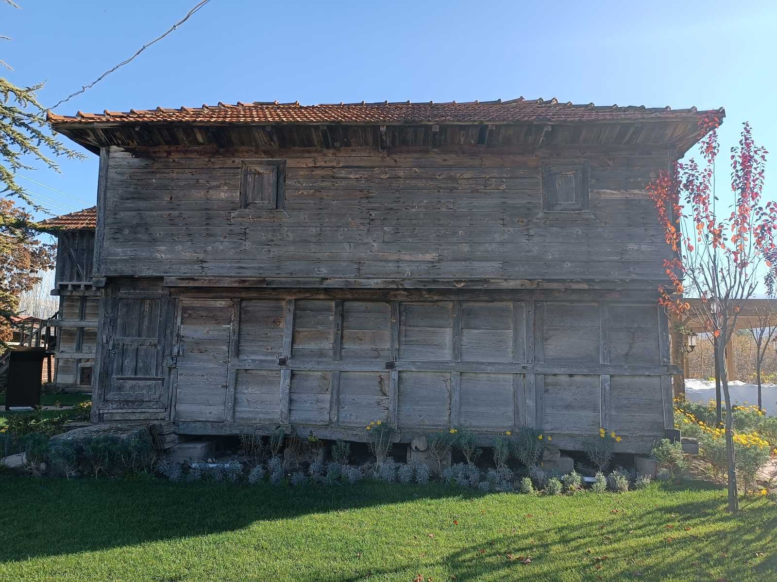 Ahşap ev, iki katlı, çatısı kırmızı kiremitli, bahçede ağaç ve çimenler