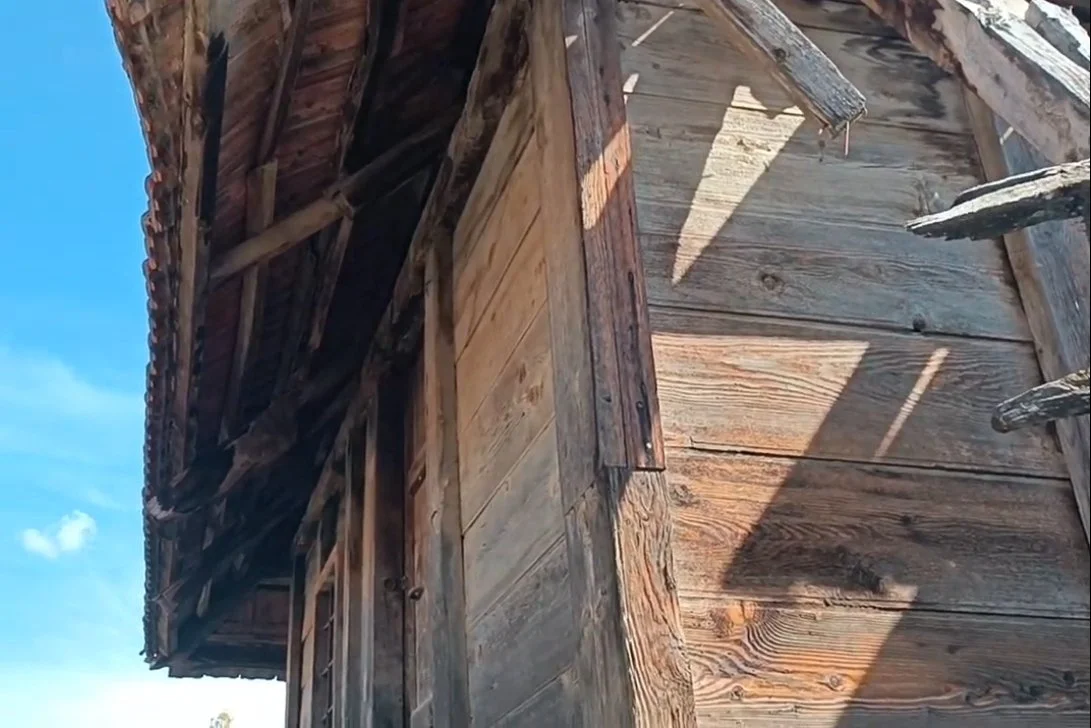 Eski ve ahşap bir kulübenin köşesi, zamanla yıpranmış ve çatlamış ahşaplar, gökyüzü açık ve mavi.