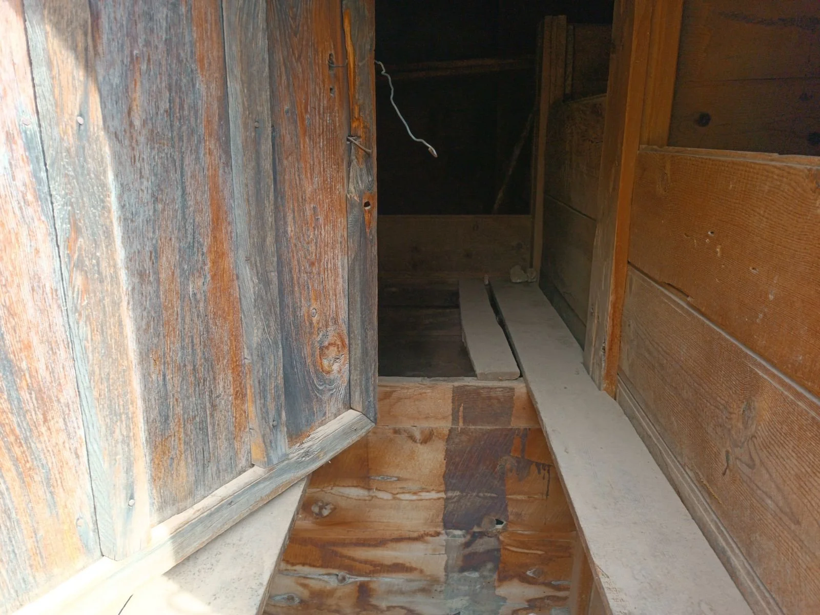 Ahşap duvarlar ve zeminle eski ve boş bir odanın içi, açık bir kapı ve karanlık bir alan görünümünde.
