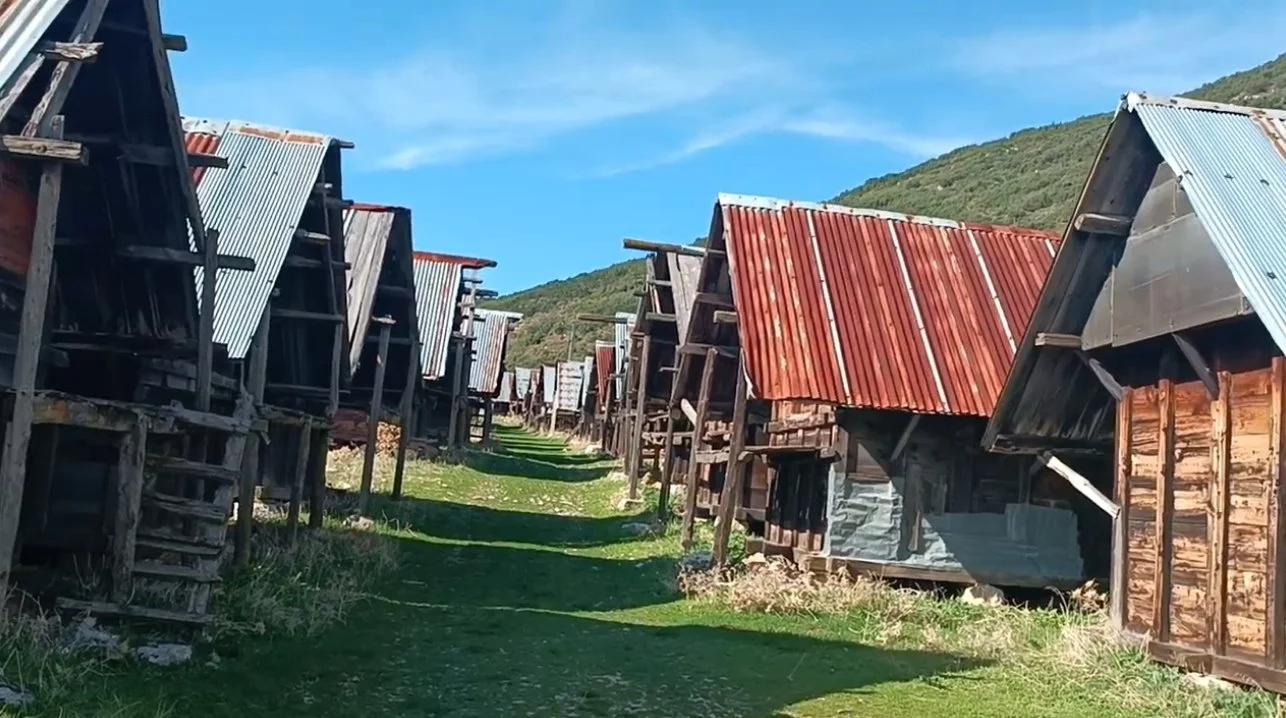 Dağlık alanda sıralanmış ahşap ve metal çatılı eski kulübeler veya barakalar.