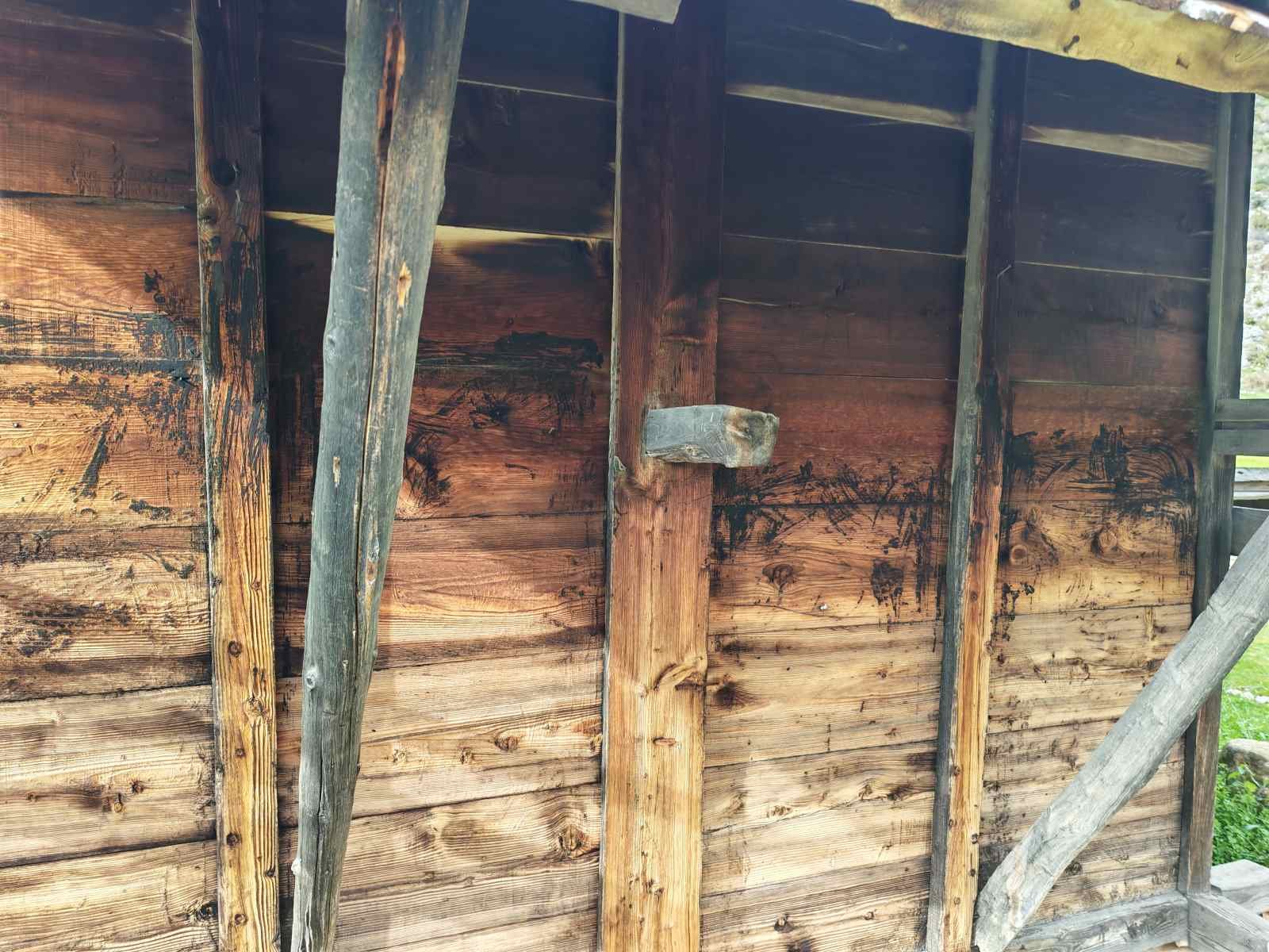 Ahşap bir kulübenin iç duvarı, çatlamış ve kararmış ahşap panellerle kaplıdır. Ortada bir duvar parçası ve birkaç yanlamasına yerleştirilmiş destek dikmesi görülüyor.