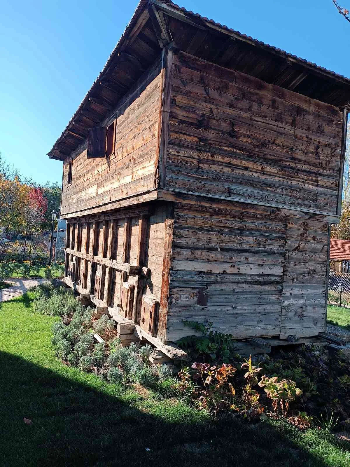 İki katlı, ahşap bir kulübe; üst kat daha büyük, alt kat daha küçük ve çıkıntı yapmış. Kulübenin etrafında yeşil çim ve çeşitli bitkiler var.