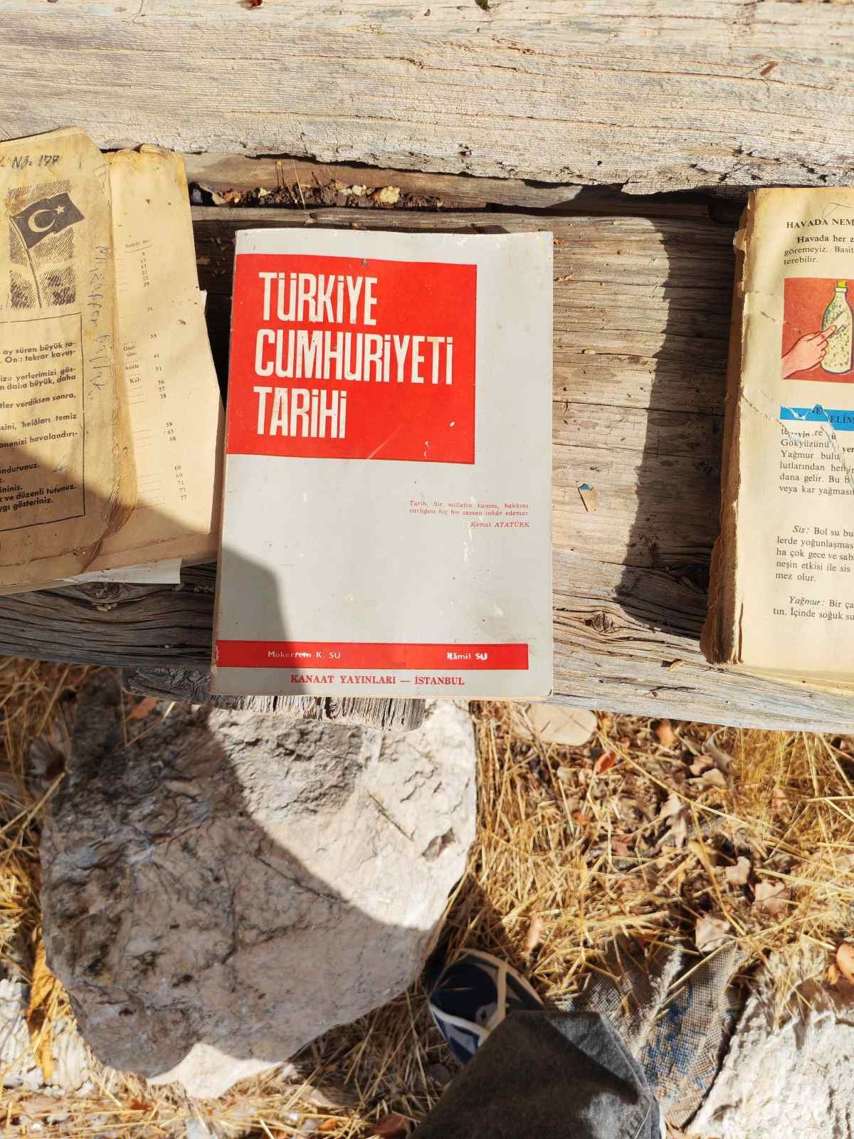 Bir kitap, Türkçe Cumhuriyeti Tarihi yazılı kırmızı ve beyaz kapaklı, diğer kitaplar ve taşların bulunduğu açık hava ortamında. 