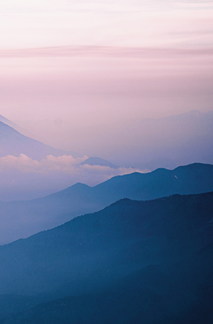 Layered mountain ranges under a pastel sky during sunrise or sunset.