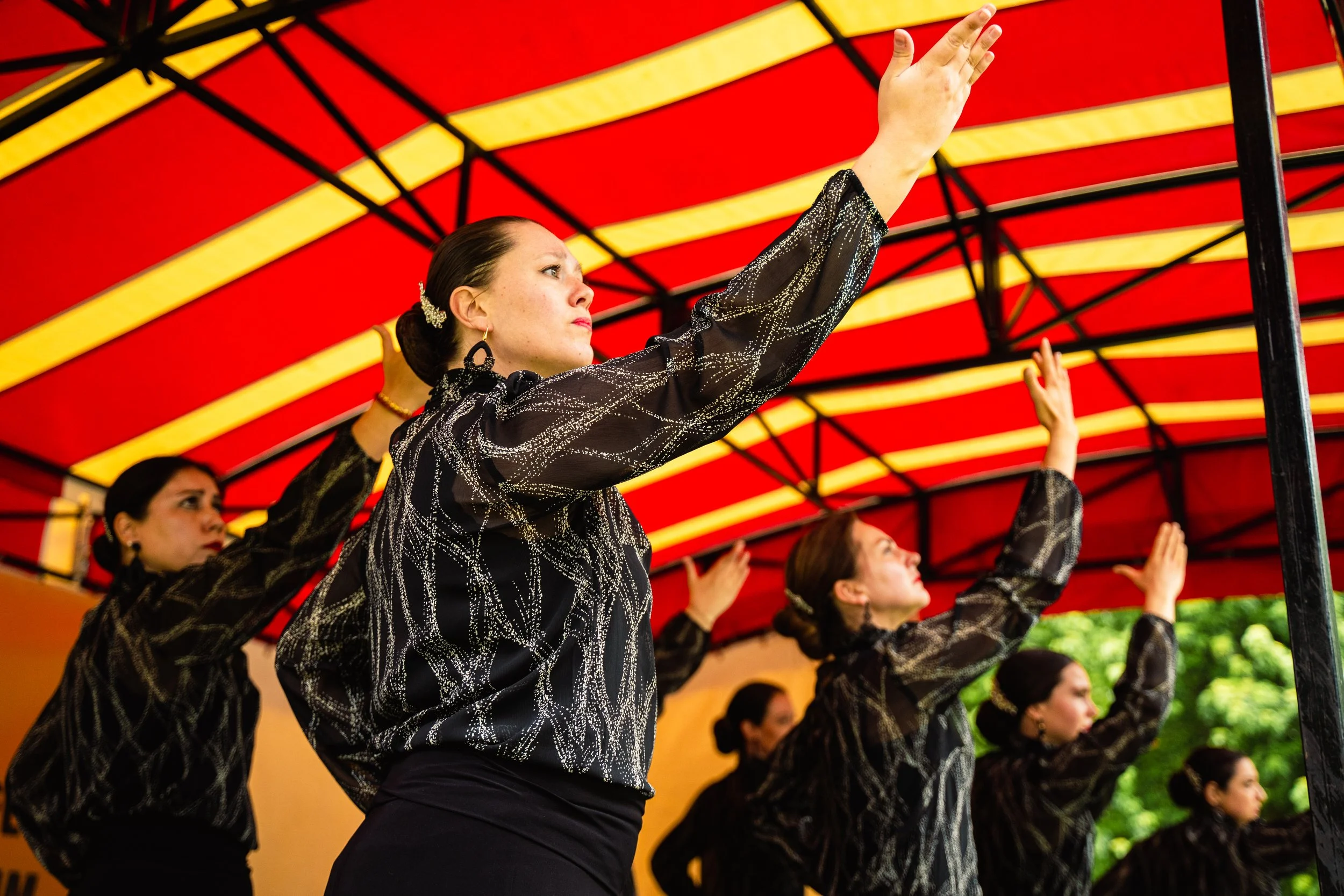 Women in black and gold blouses performing a traditional dance under a decorated red and yellow canopy.