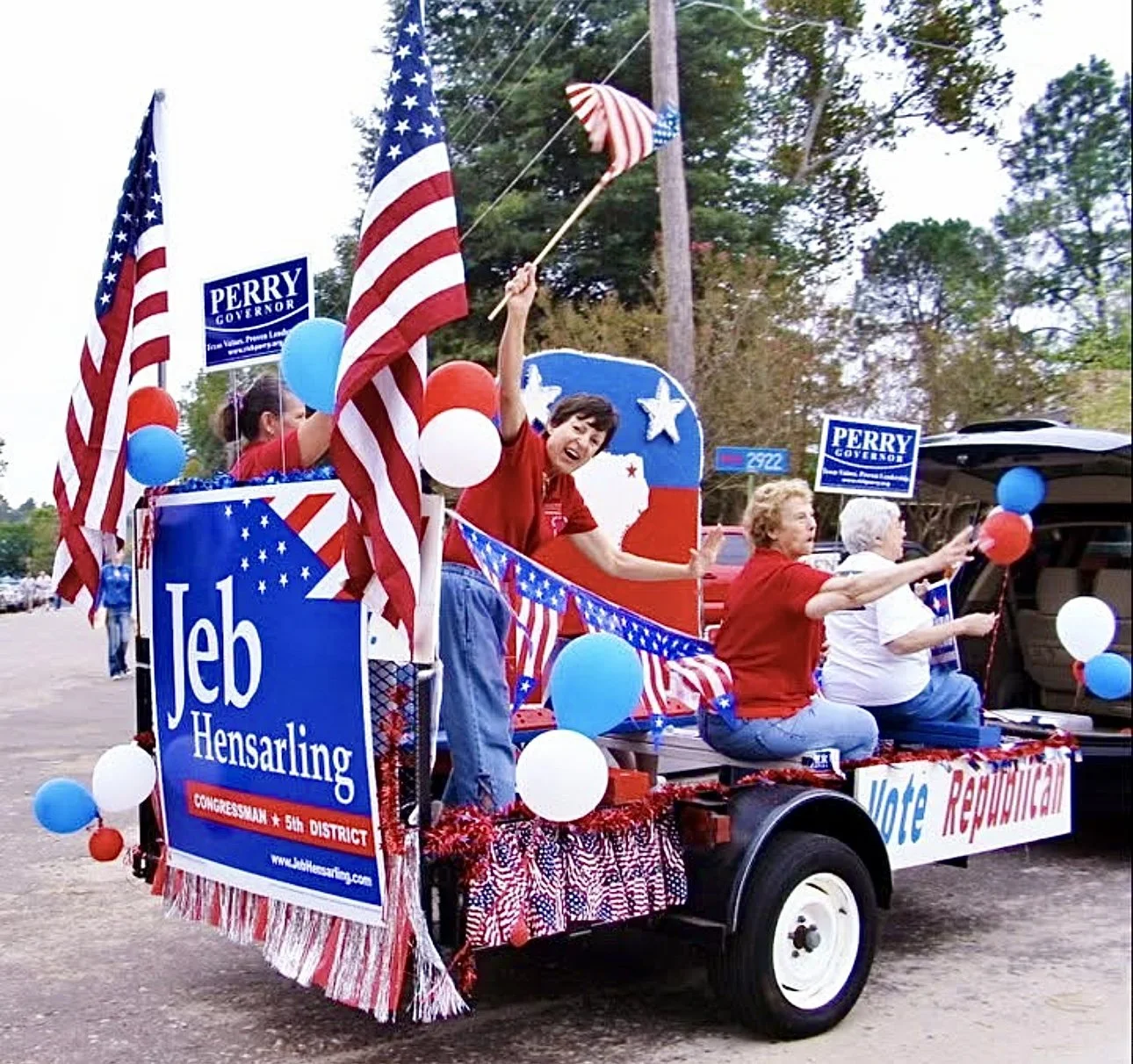 A parade float decorated with American flags, balloons, and signs supporting Jeb Hensarling and Perry Governor, featuring people waving and promoting vote Republican.