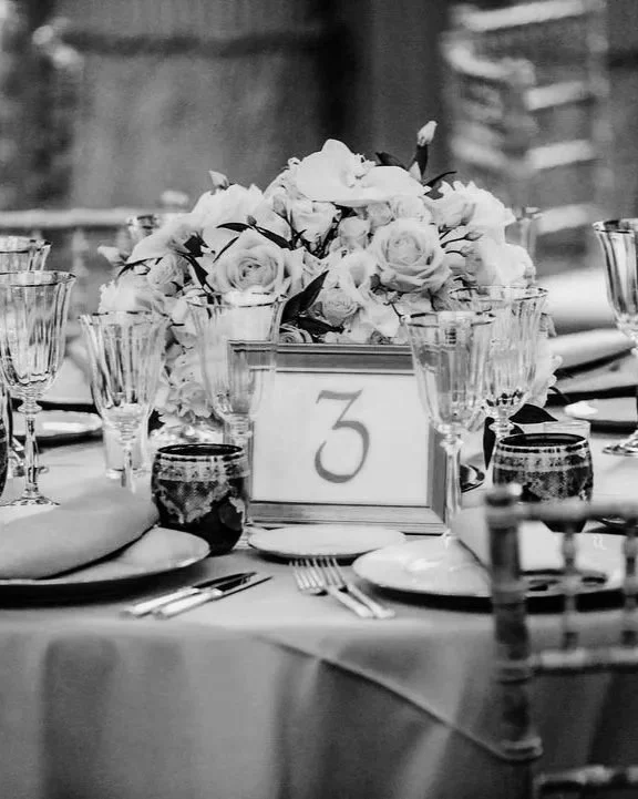 Une table de fête avec un centre de table de fleurs, des verres à vin, des assiettes, des couverts, une carte de table avec le numéro 3, dans un décor d'événement ou de réception.