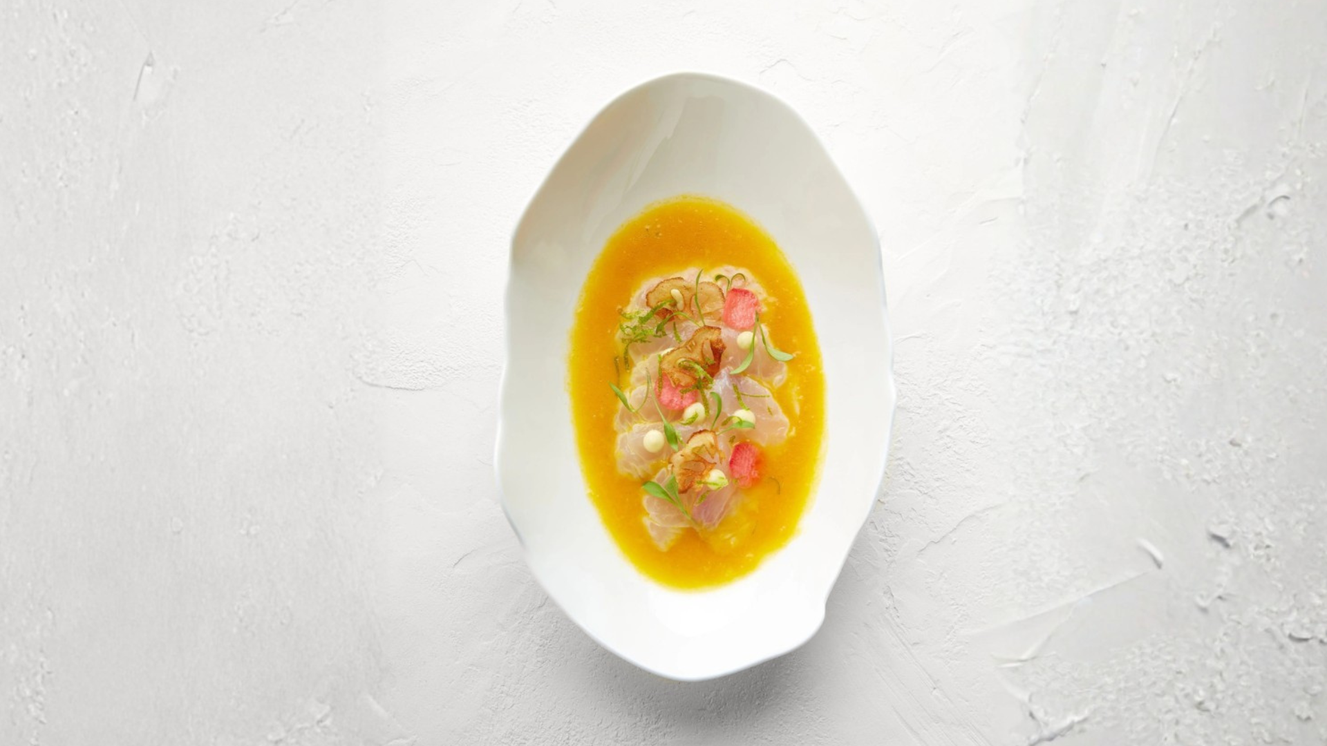 Soupe de poisson servie dans un bol blanc avec des garnitures de légumes, herbes et petits morceaux de poisson.