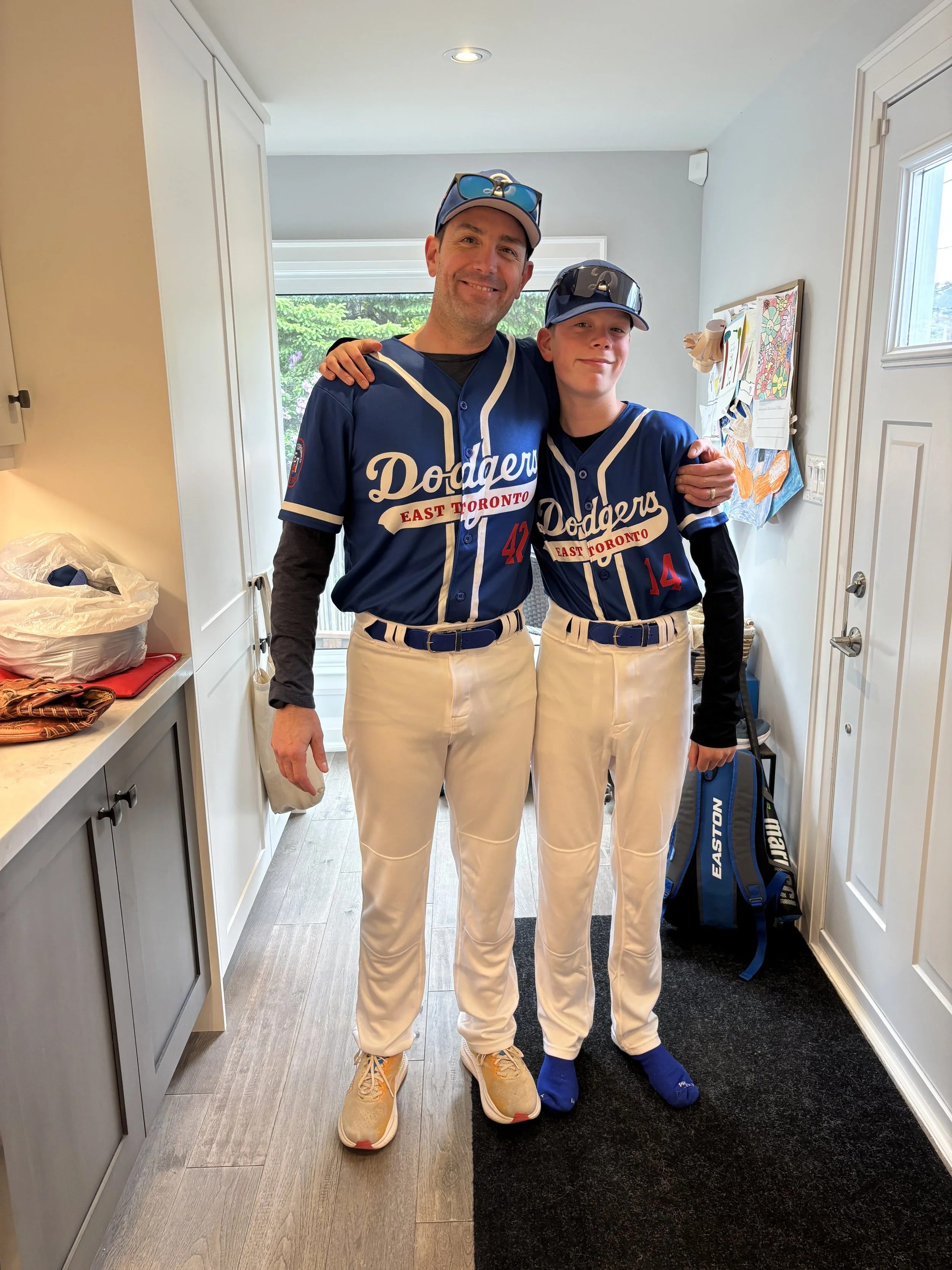 Image of Jason Magennis and his son, wearing baseball uniforms, prior to leaving for a baseball game. Jason is a active youth baseball coach.