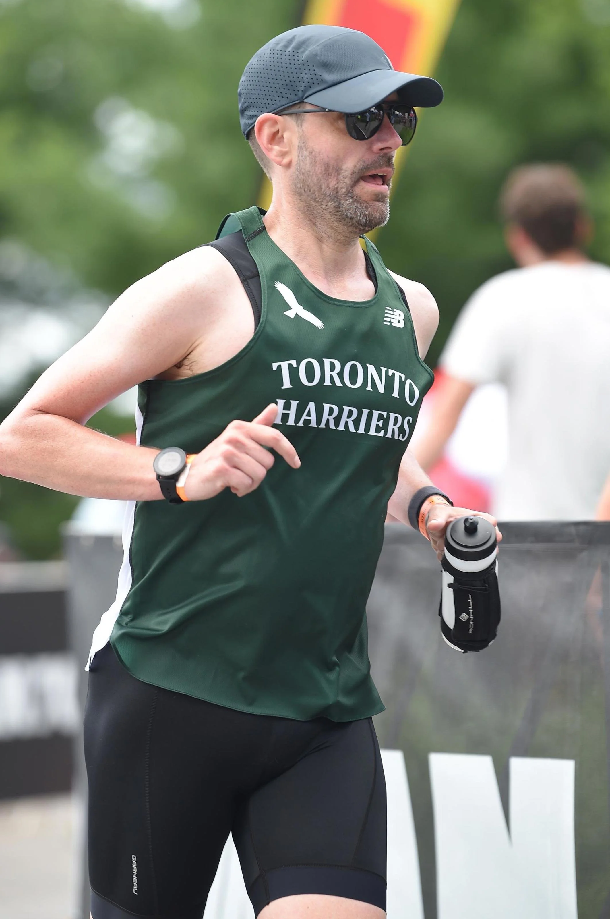 Image of Jason Magennis, high performance coach, wearing his Toronto Harriers singlet, as he rounds the corner in the final stage of the Muskoka Ironman 70.3 race.