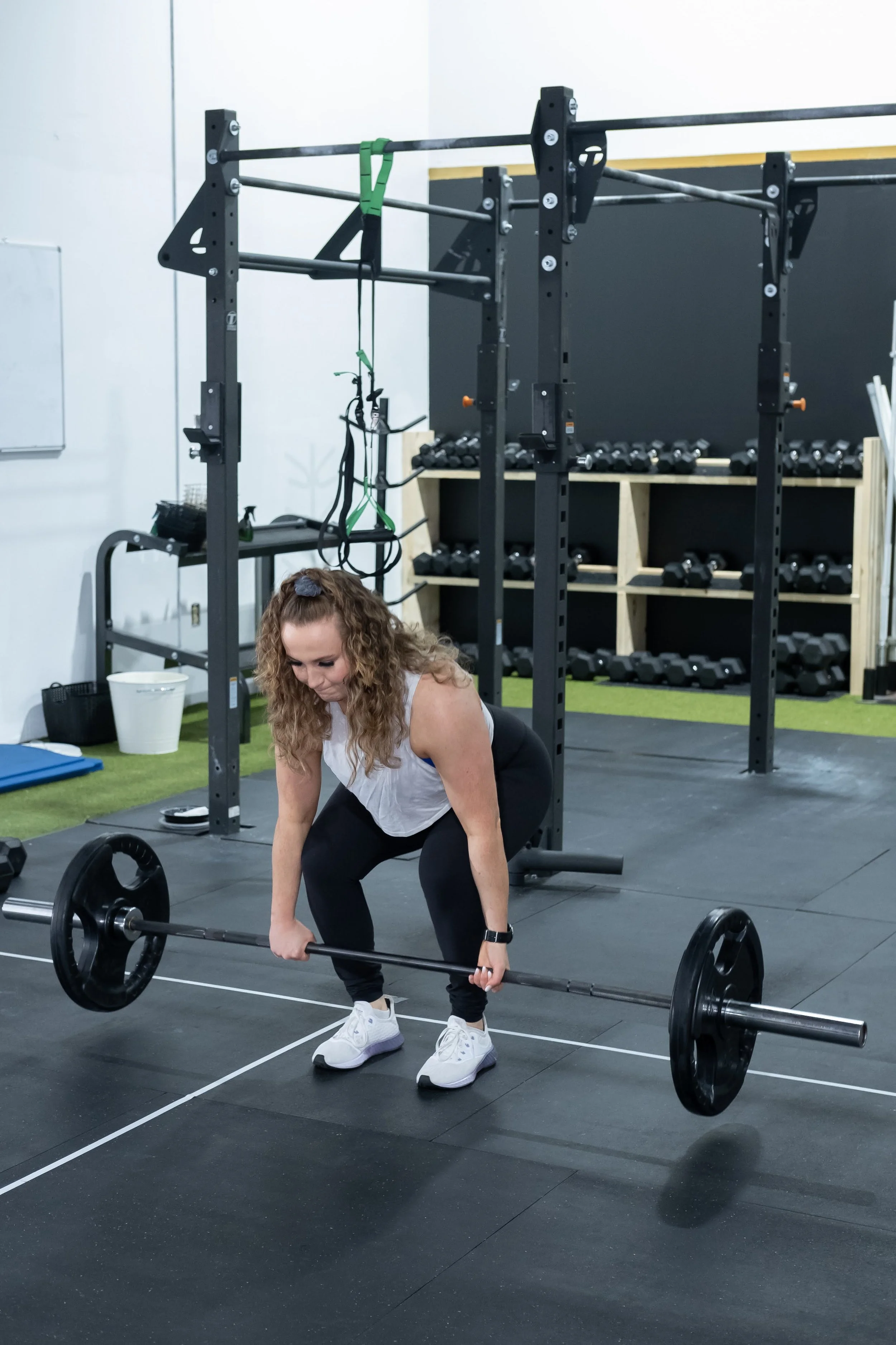 A woman in workout clothes performing a deadlift with a barbell in a gym.