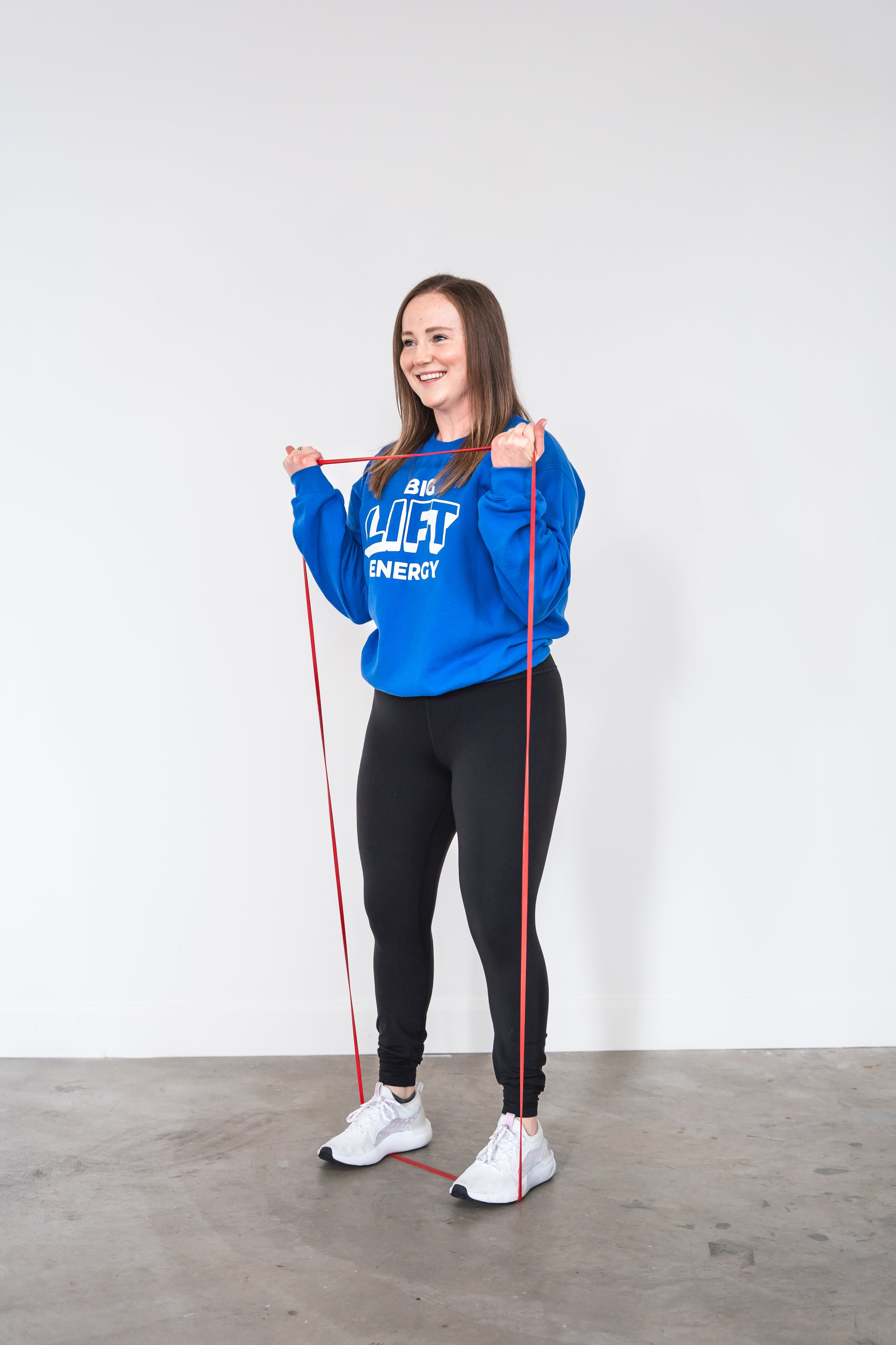 A strength coach for women in Cambridge Ontario doing holding a resistance band wearing a blue crewneck and black joggers.