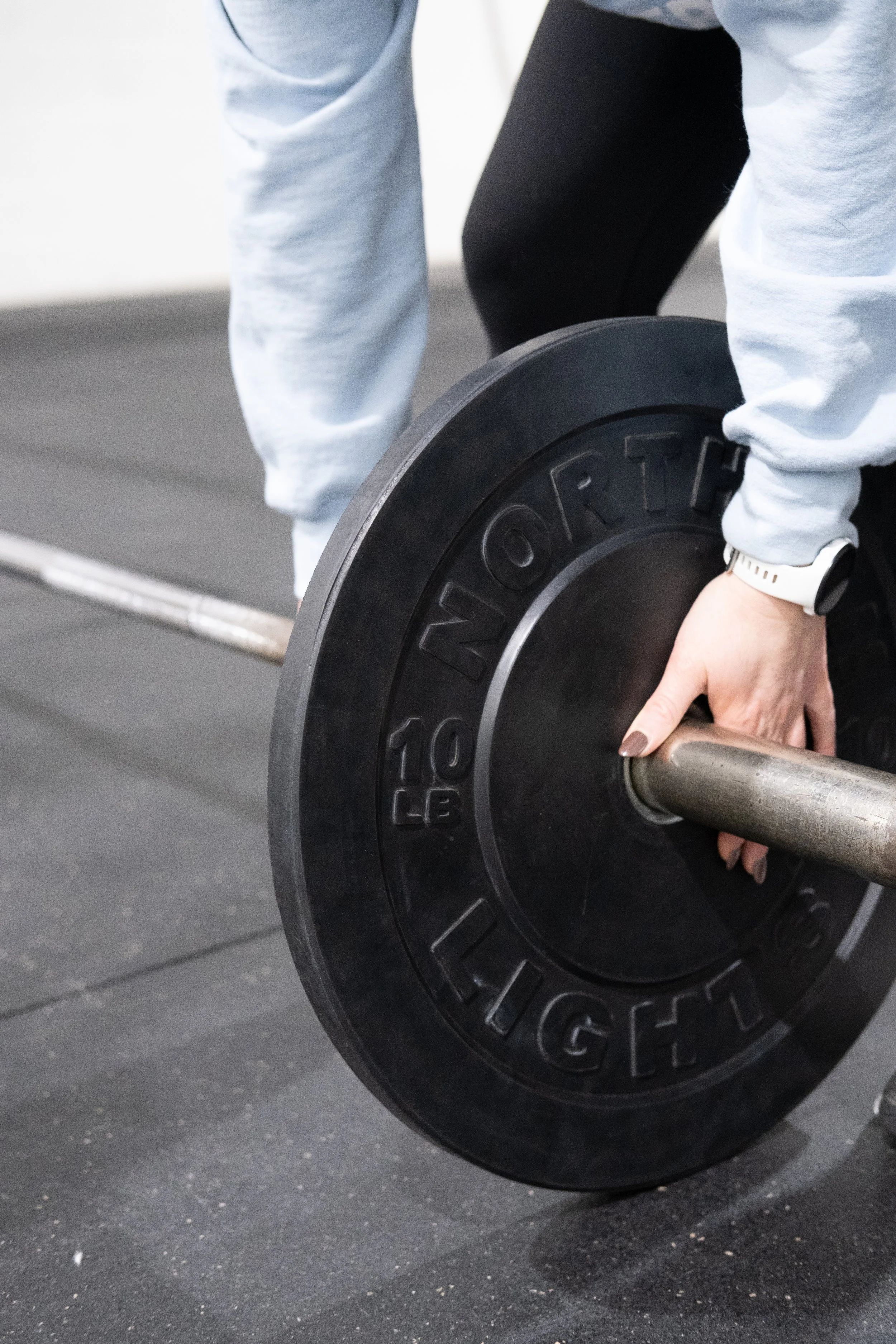 Brantford Ontario women's strength coach's arms holding a barbell with weights in a private gym.