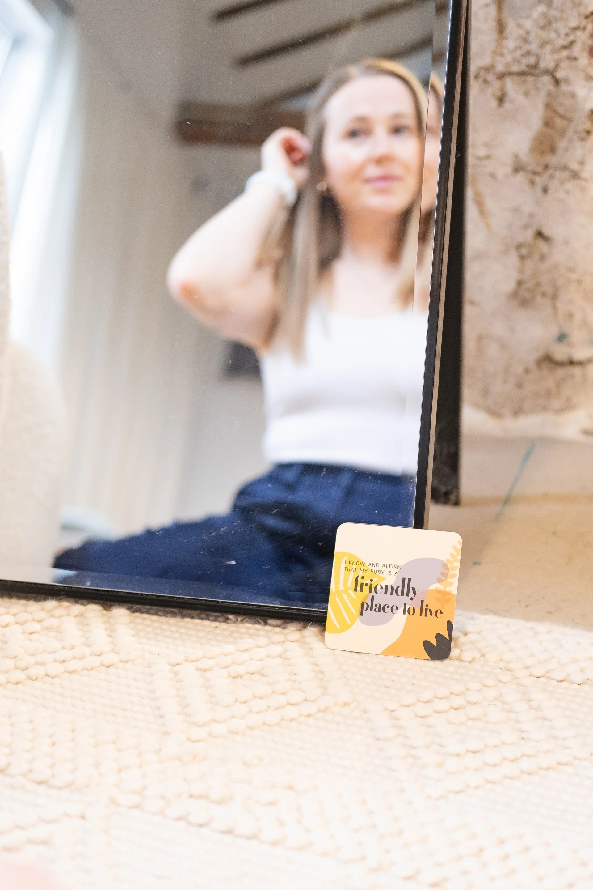 Female group fitness trainer near Hamilton Ontario looking into a mirror with an affirmation card in Brantford.