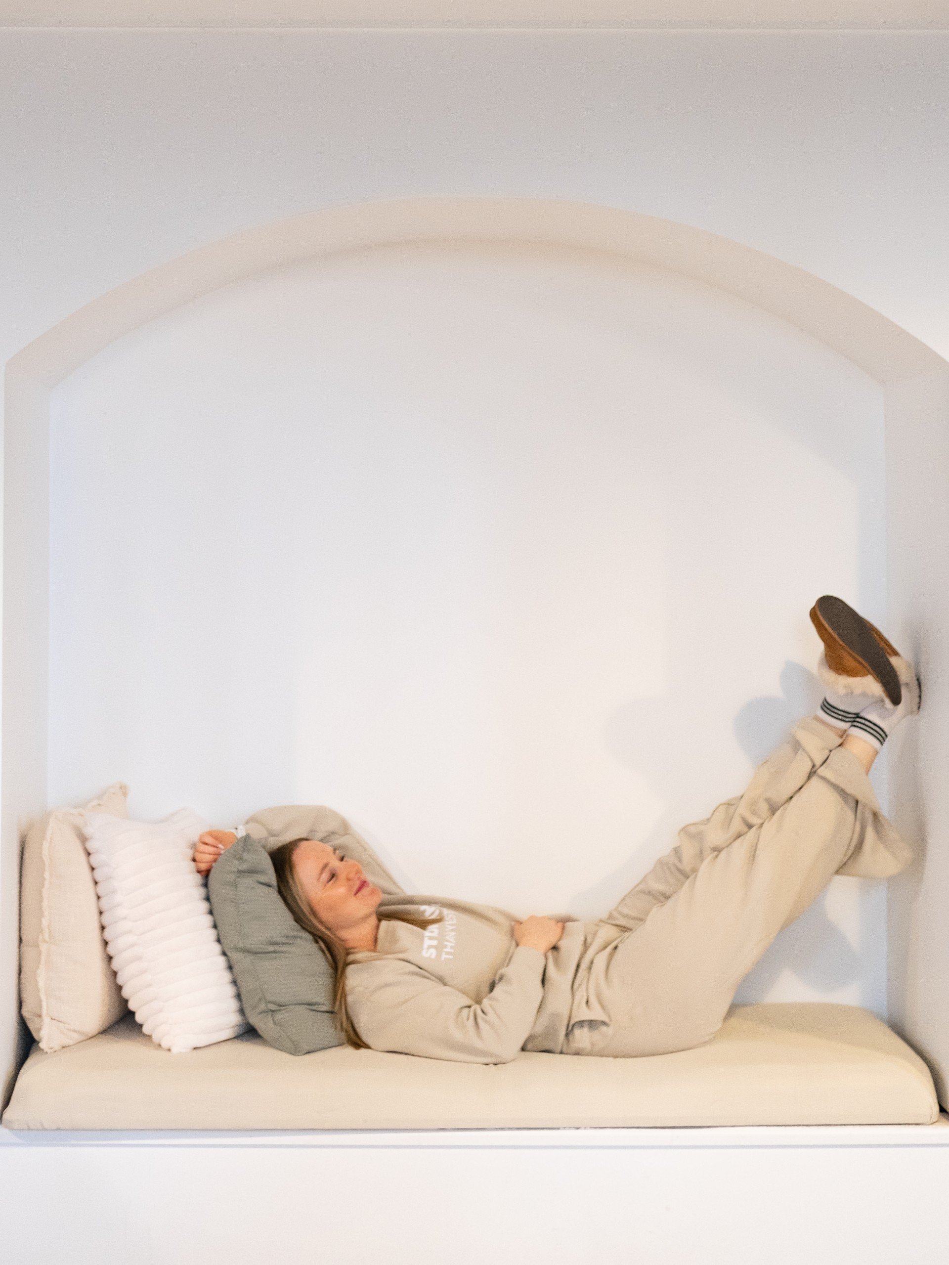 Female strength trainer for women in Brantford Ontario laying in beige sweatsuit in a comfy nook with her feet up