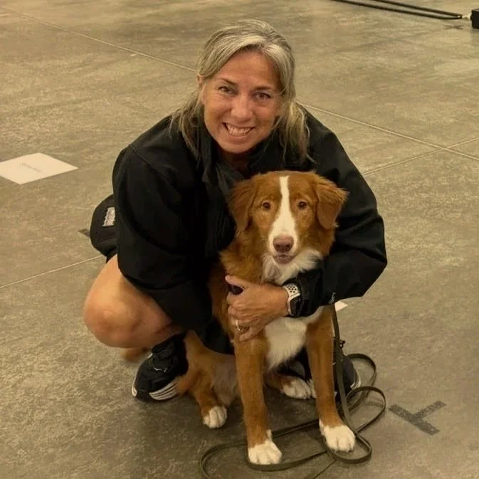 A woman crouched over and hugging a Nova Scotia Duck Tolling Retriever