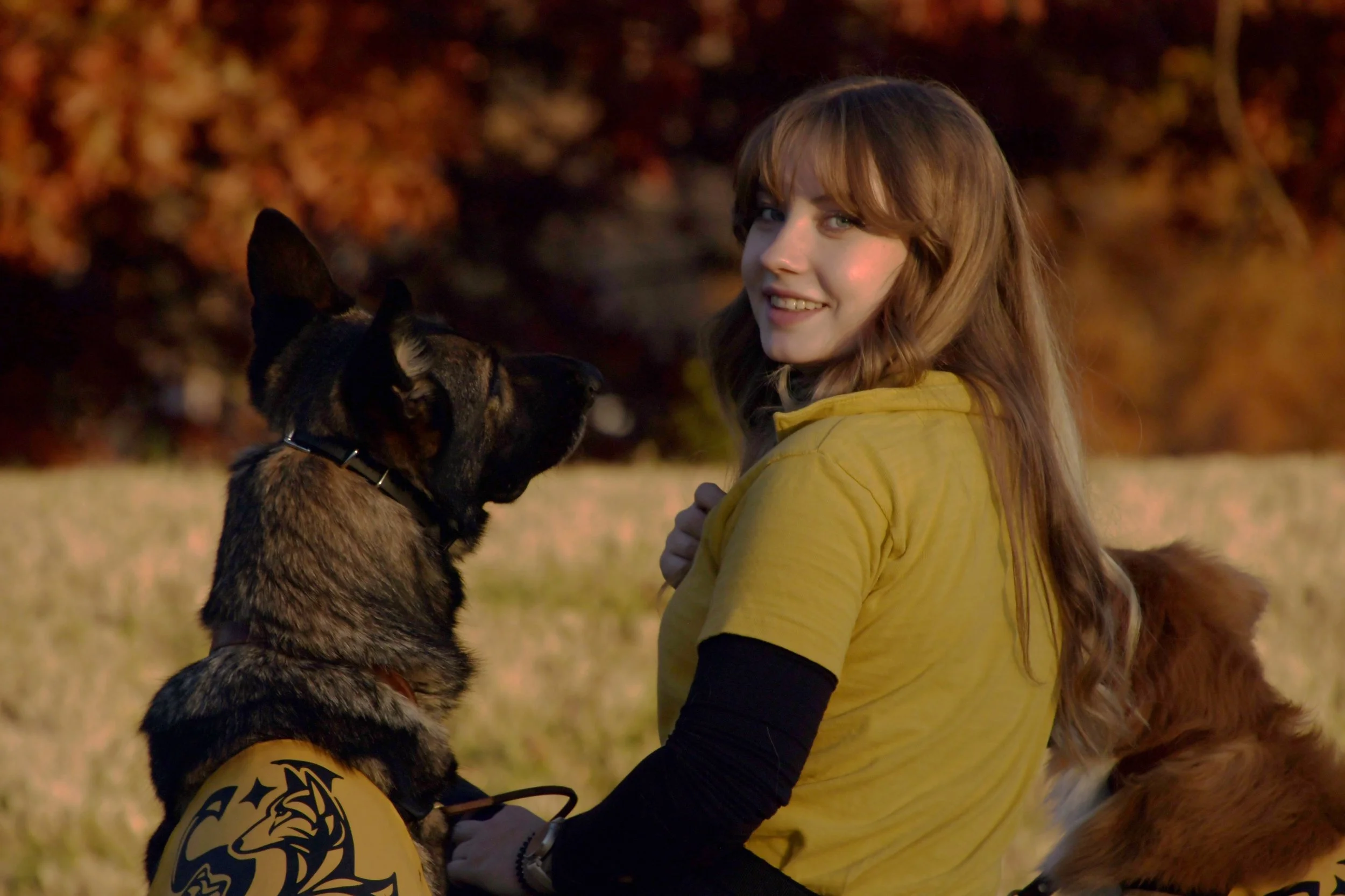 A young woman with red hair and a yellow jacket smiling and holding the face of a large, spotted dog.