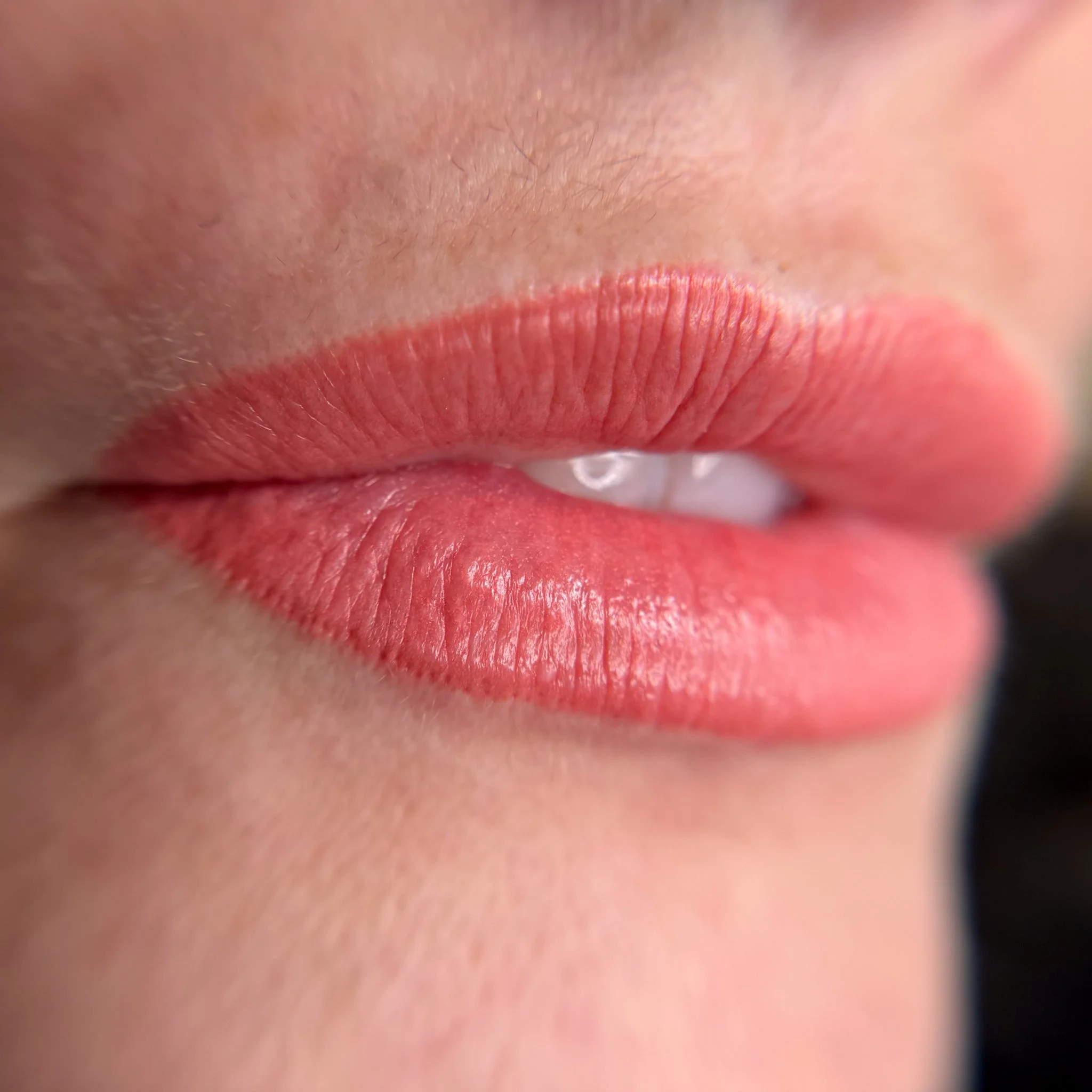 Close-up of a person's lips with pink lipstick, slightly parted, showing a hint of teeth.