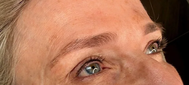 Close-up of a woman's face, focusing on her eyes and eyebrows, with light-colored hair and blue eyes.
