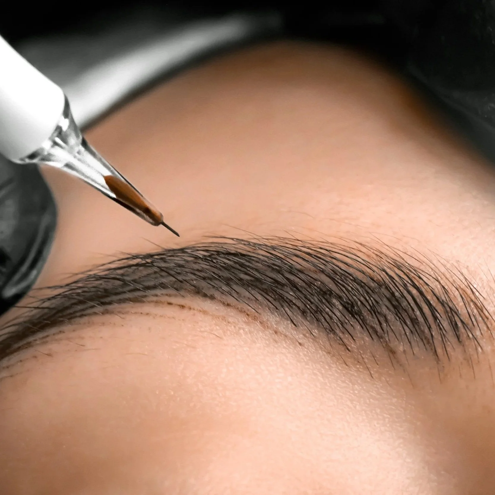 Close-up of a person's eyebrow being treated with a microblading pen during a cosmetic procedure.