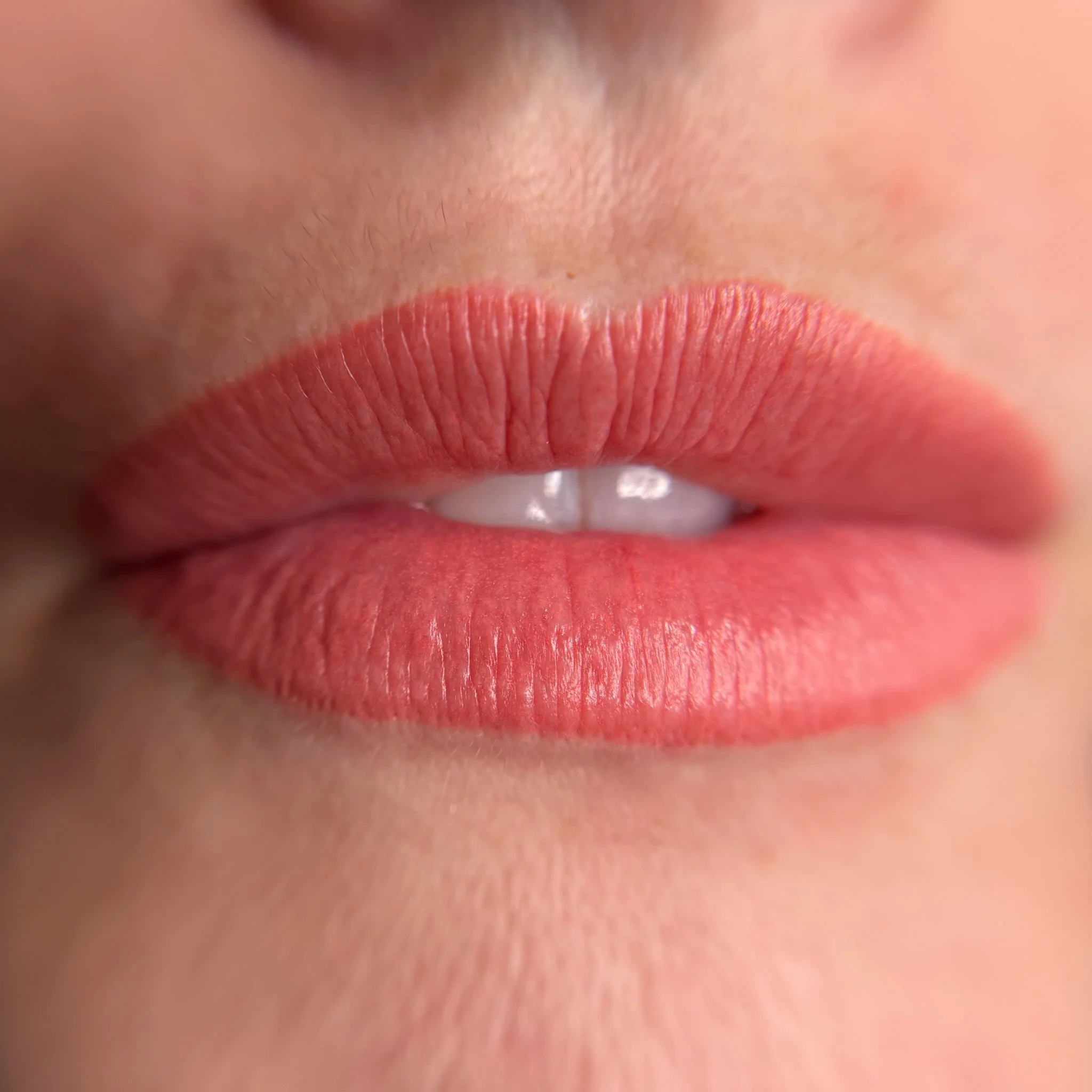Close-up of partially open lips with pink lipstick and visible teeth.