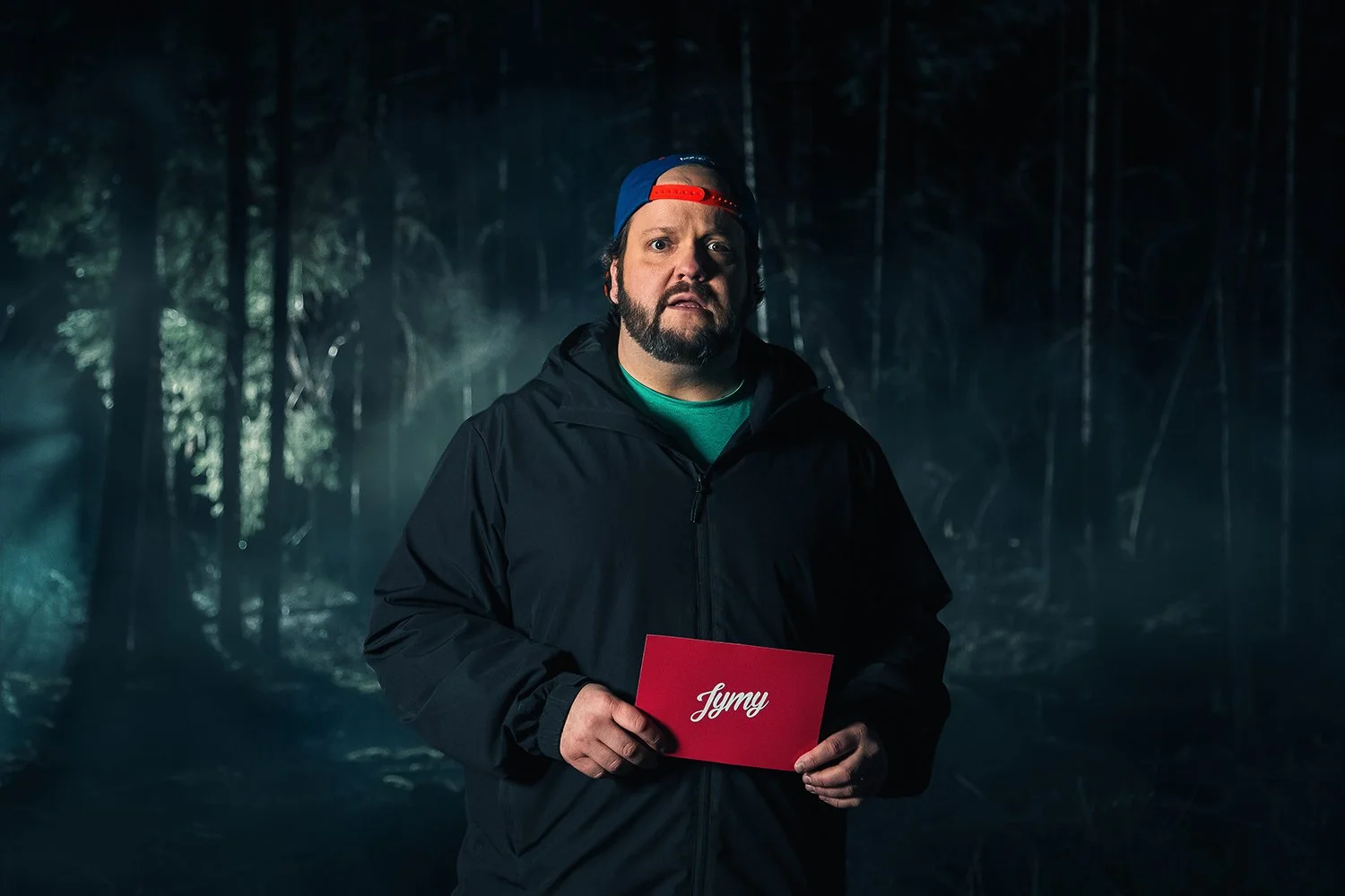 Mies seisoo pimeässä metsässä, pitää punakantista kirjaa jonka päällä on nimi "Jymy"