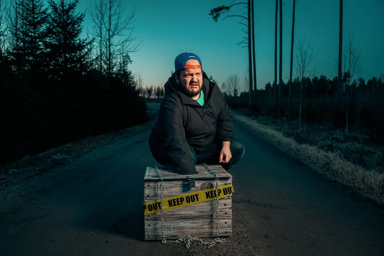 Mies on polulla, ympärillä puita ja tie, laittaa loukkuun, jonka ympärille on keltainen 'Keep Out' -tahra.