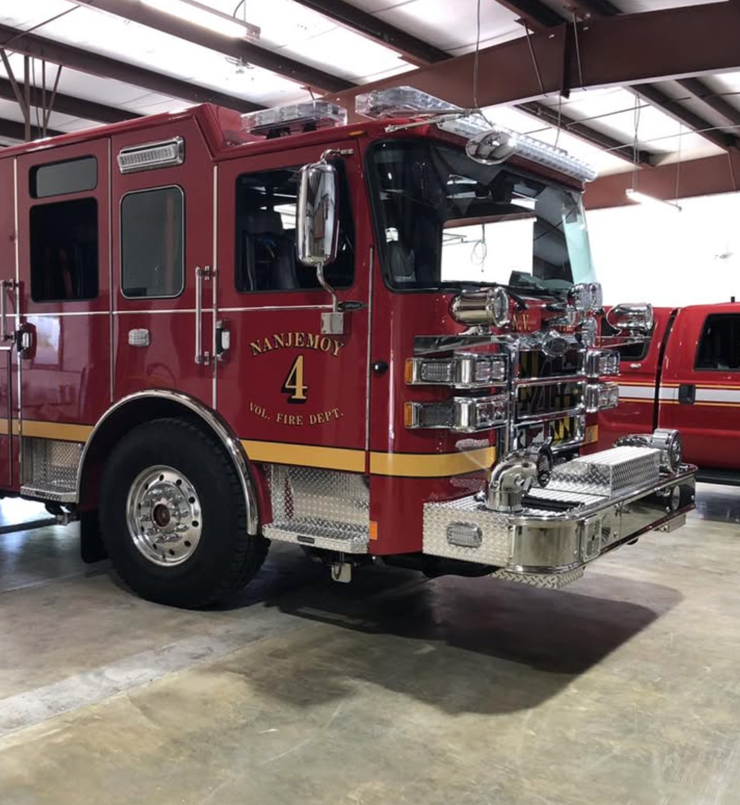 A red fire truck with chrome fixtures and a yellow stripe, labeled 'Nanjemoy Vol. Fire Dept. 4,' parked inside a warehouse-like building.