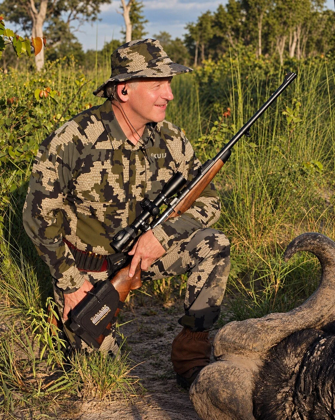 Steve on safari, kneeling with a rifle beside a buffalo
