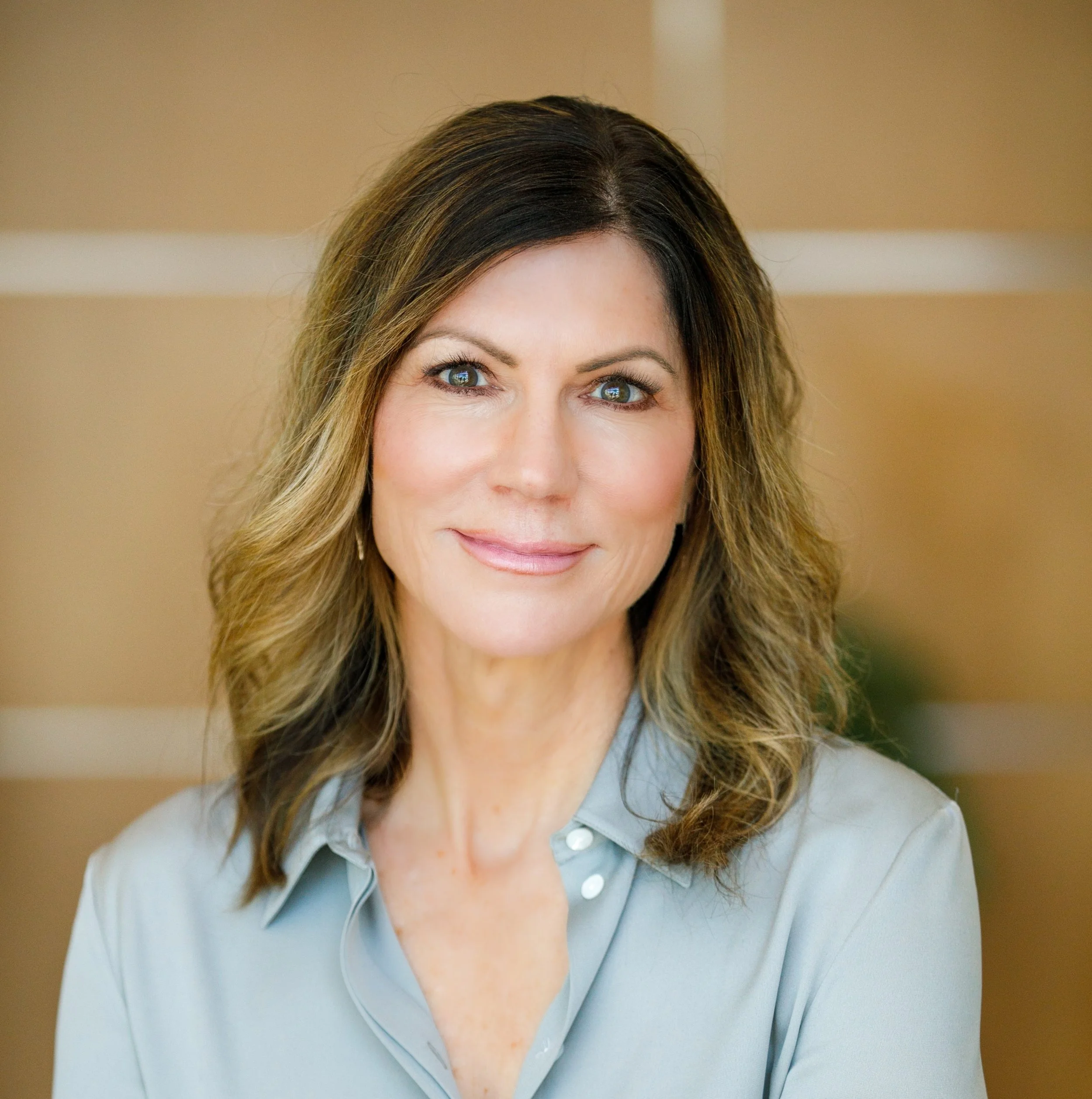 A woman with wavy brown hair and blue eyes smiling in an office setting.