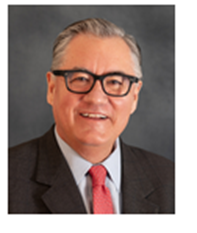 Portrait of a smiling man with gray hair, wearing glasses, a dark suit, white shirt, and red tie, against a gray background.
