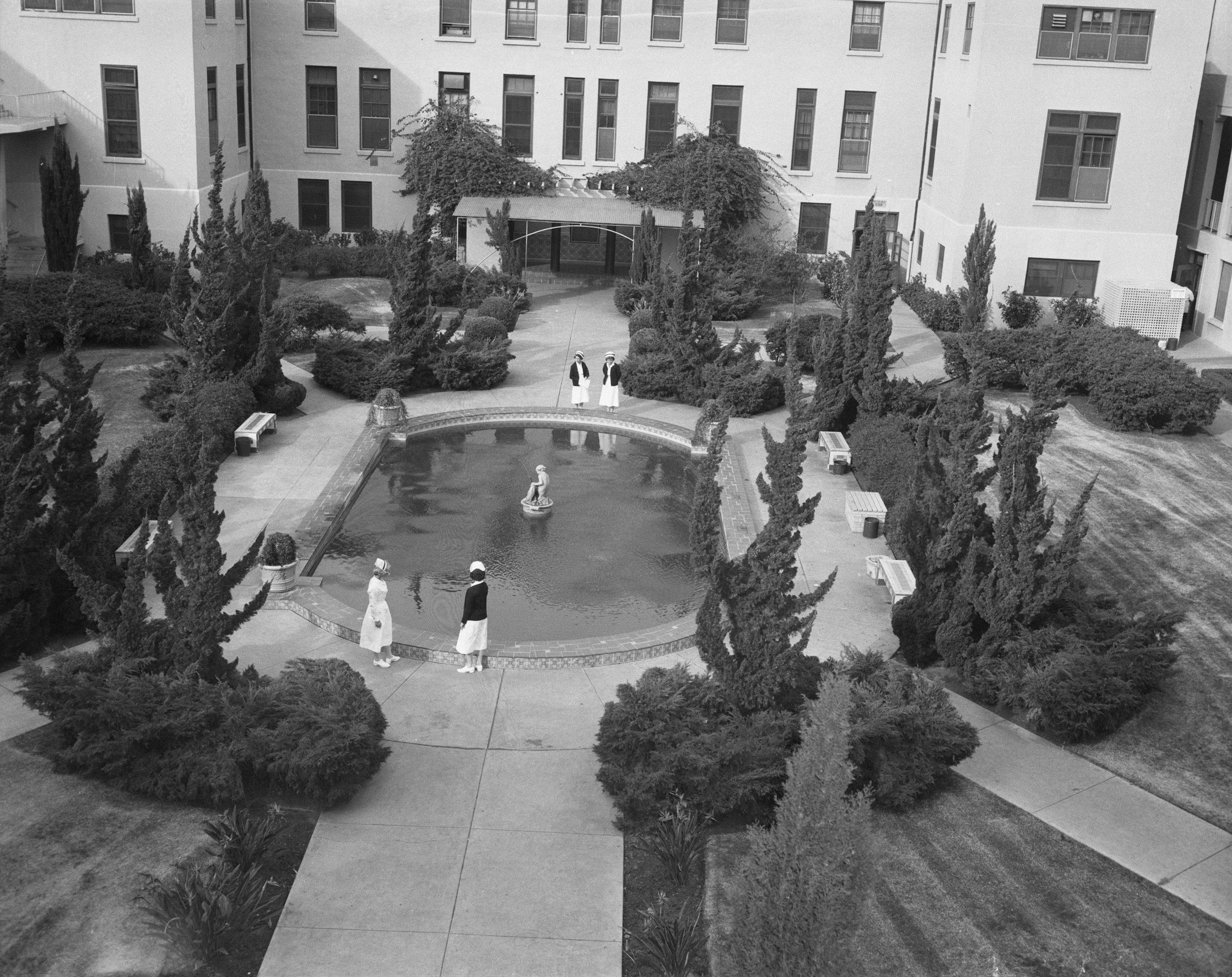 A historic black-and-white photo of an institutional medical or research facility courtyard, with people walking and gathering-visually reinforcing the history of medical research.
