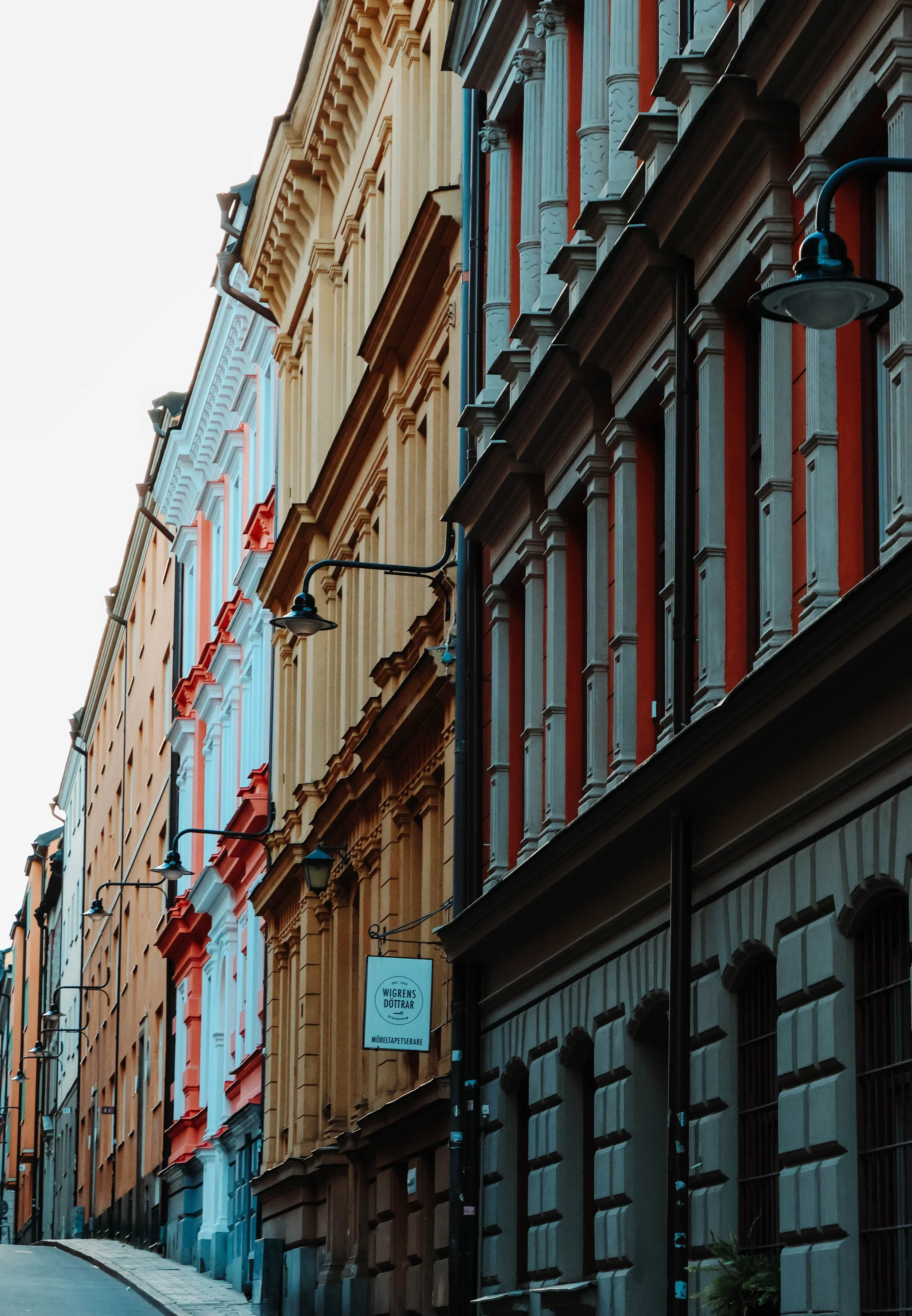 Painted facades and the hush of fall.
The narrow street climbs gently, framed by buildings dressed in warm tonesâorange, ochre, and faded blueâlike autumn leaves frozen in time. The air is crisp, the light soft, and the city feels like it's holding