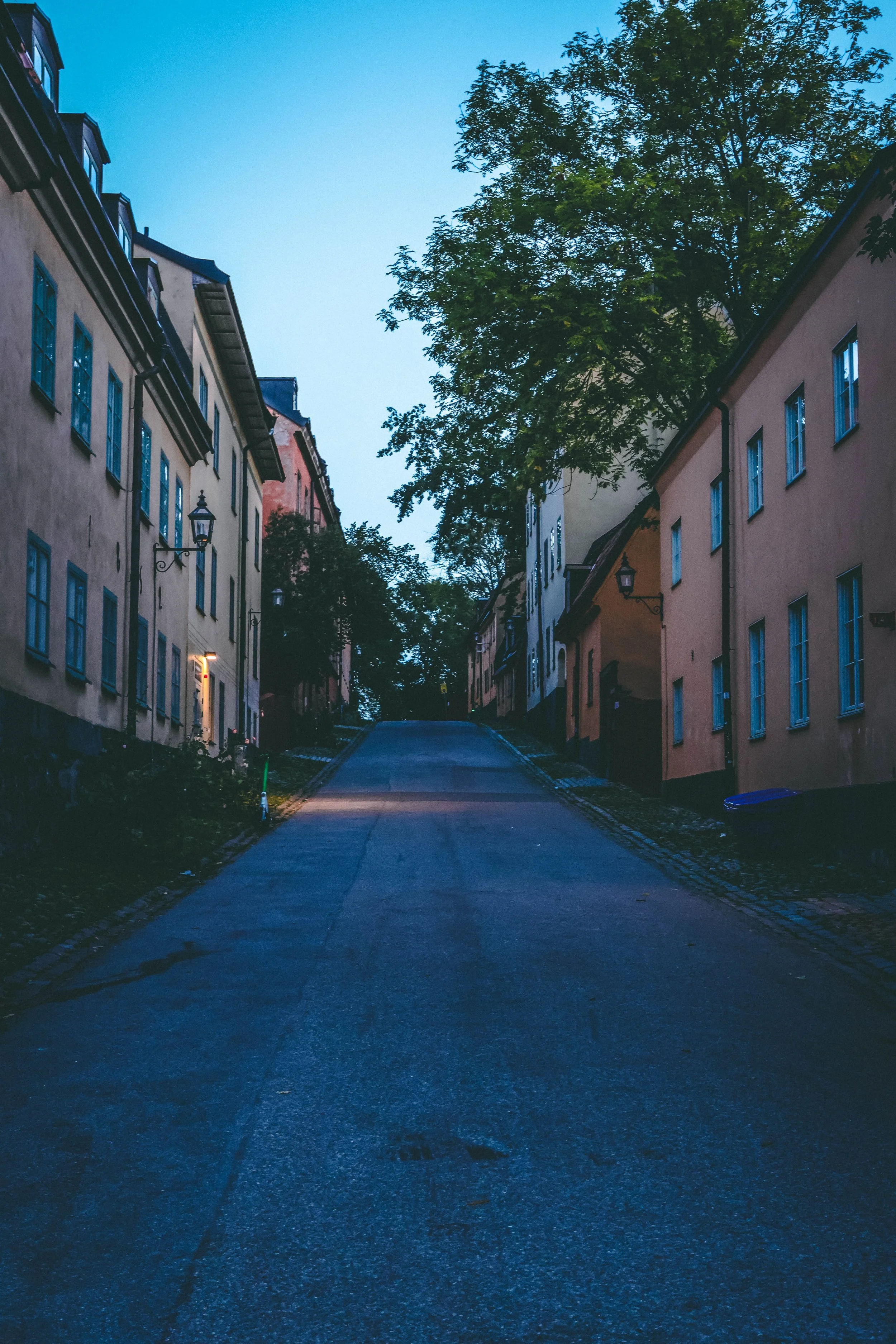 A beacon in the hush of dawn.
The street sleeps under a crisp autumn sky, its pastel walls still wrapped in dreams. But one entrance light glows softlyâwelcoming, watchful, perhaps waiting. Itâs not just illumination; itâs a quiet invitation to wond