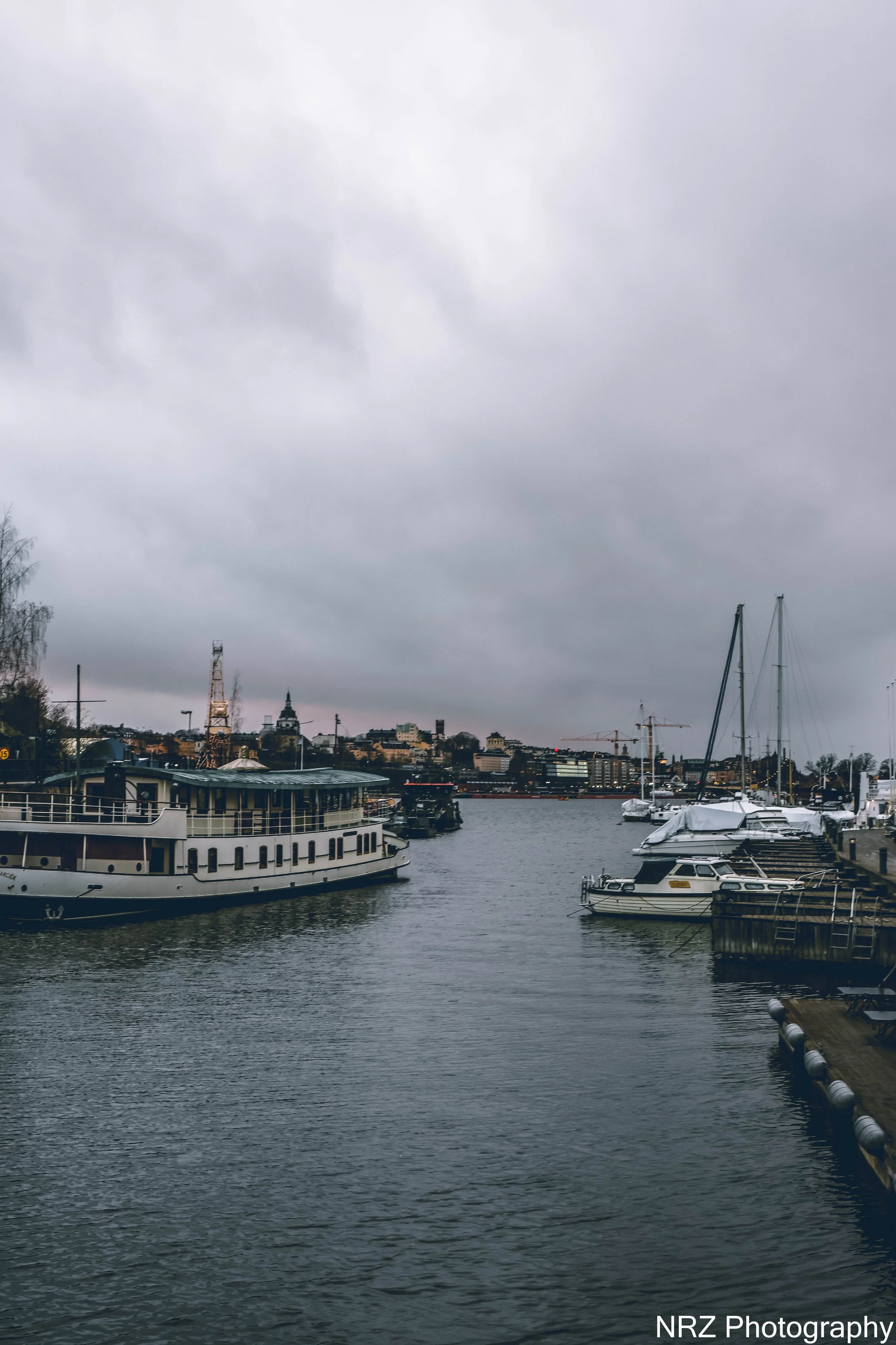 “Hamnen vid världarnas rand” – berättat av Olle, ugglan
Jag landade på en lyktstolpe vid kajen, vingspetsarna fuktiga av dimma. Vattnet låg stilla, som om det höll andan, och båtarna sov med sina segel tätt lindade. Himlen var grå, men inte tom – den