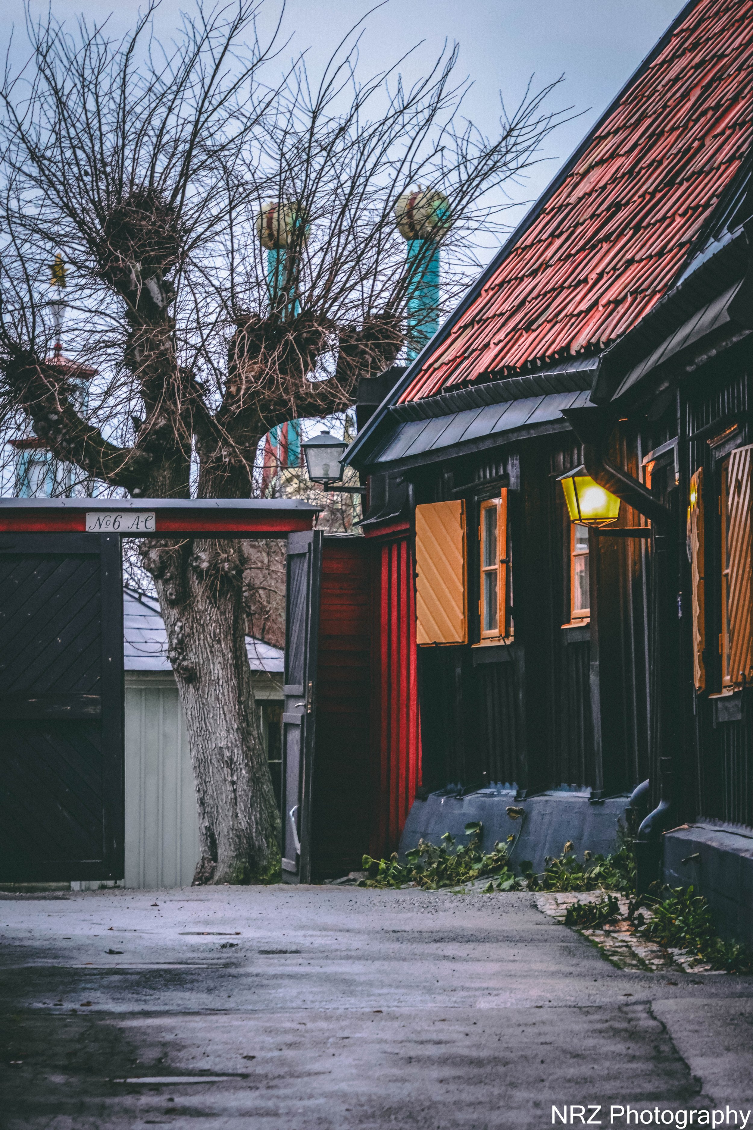 Stugans vinterhjärta
I en undanskymd gränd i Djurgårdsstaden står en liten mörk stuga, som om den själv valt att gömma sig från världen. Utanför ligger snön tung över kullerstenen, lyktans sken darrar i vintermörkret och träden står nakna som väktare