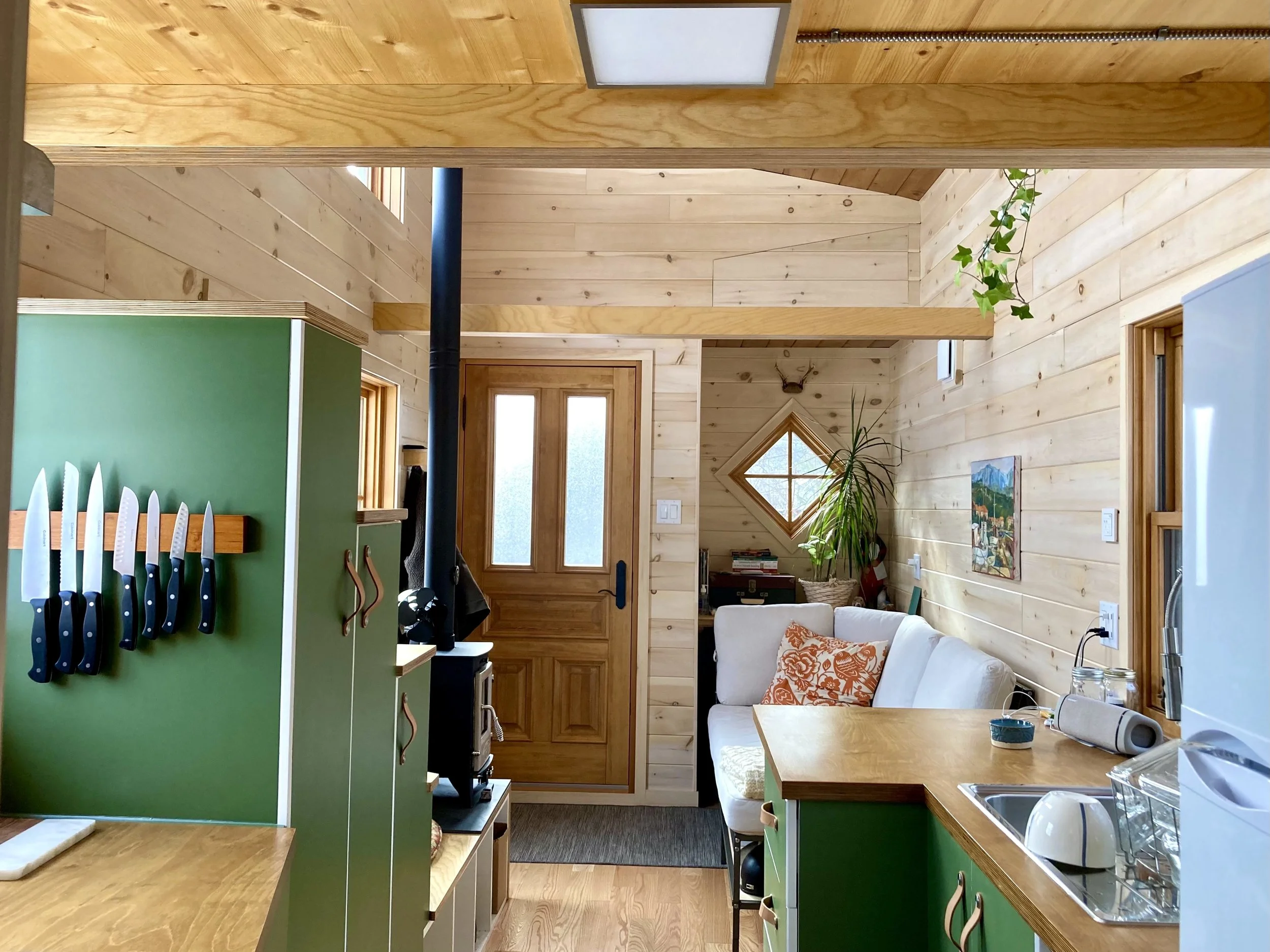 Tiny house interior with pine walls, tiny fireplace, diamond window, and green custom staircase cabinets