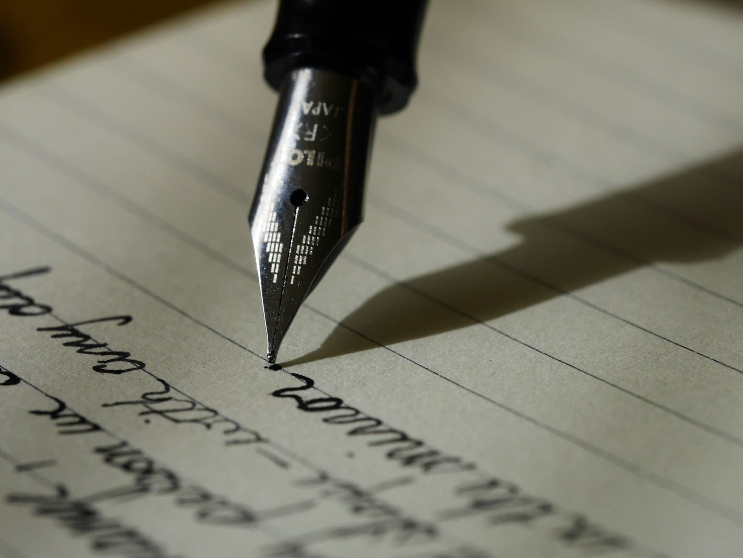 A close-up of a fountain pen writing cursive text on lined paper.