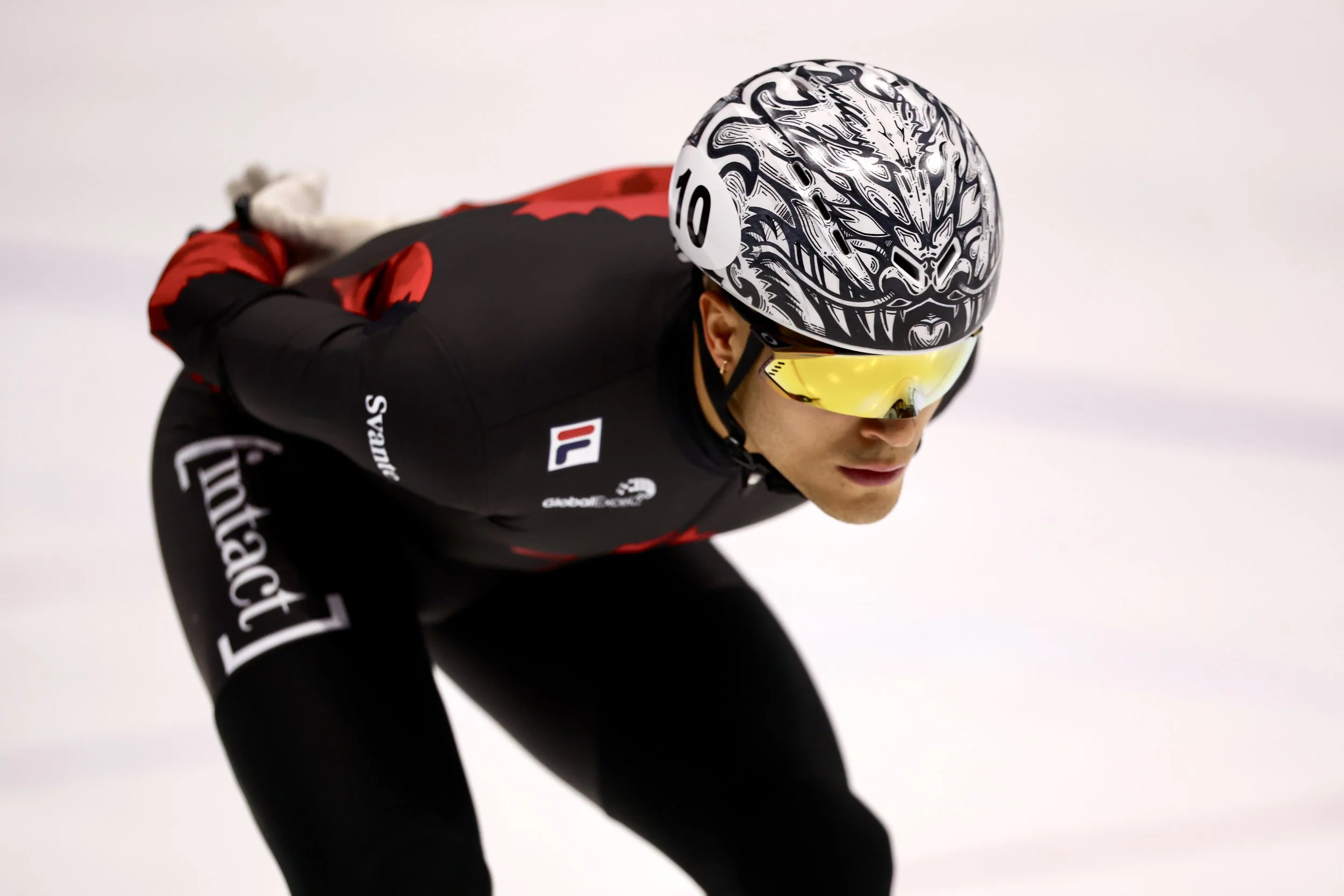 Un coureur de vitesse portant un casque à visière jaune et un maillot noir, en position de départ, sur une piste de patinage rapide.