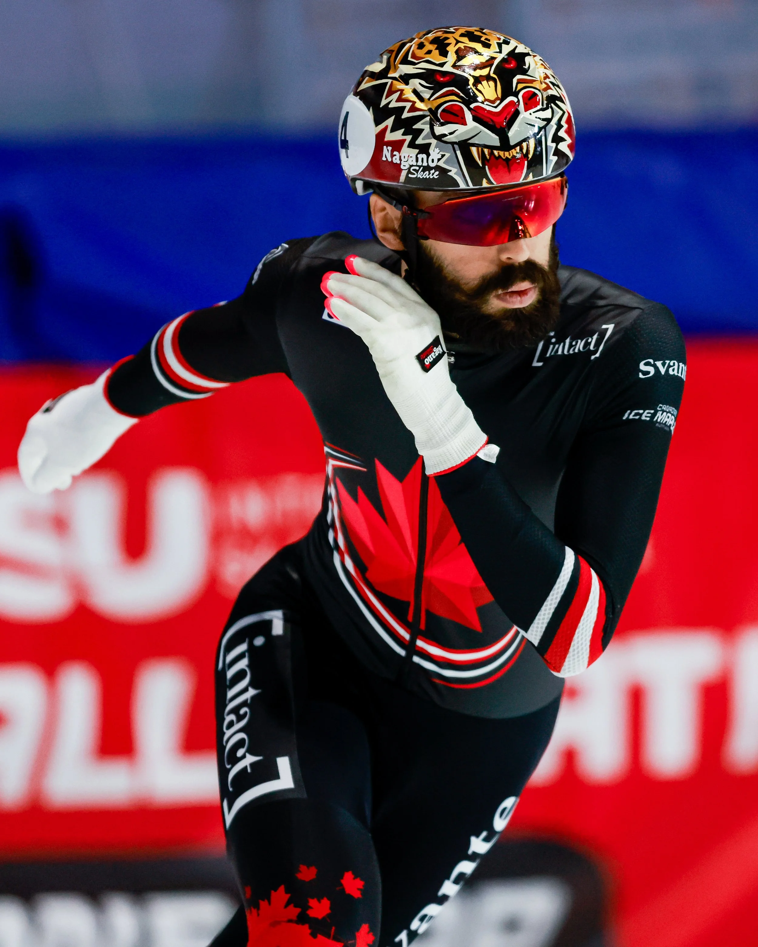 Un skieur en plein effort portant un casque décoré d'un tigre et des lunettes de protection rouges, vêtu d'une combinaison noire avec des détails en rouge et blanc, lors d'une compétition.