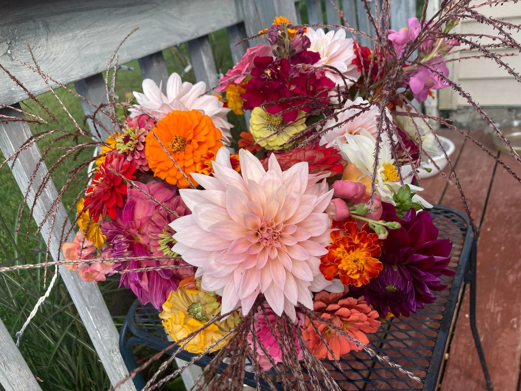 Colorful bouquet of flowers including dahlias, marigolds, zinnias, and other seasonal flowers on a black metal table outdoors near a wooden bench.